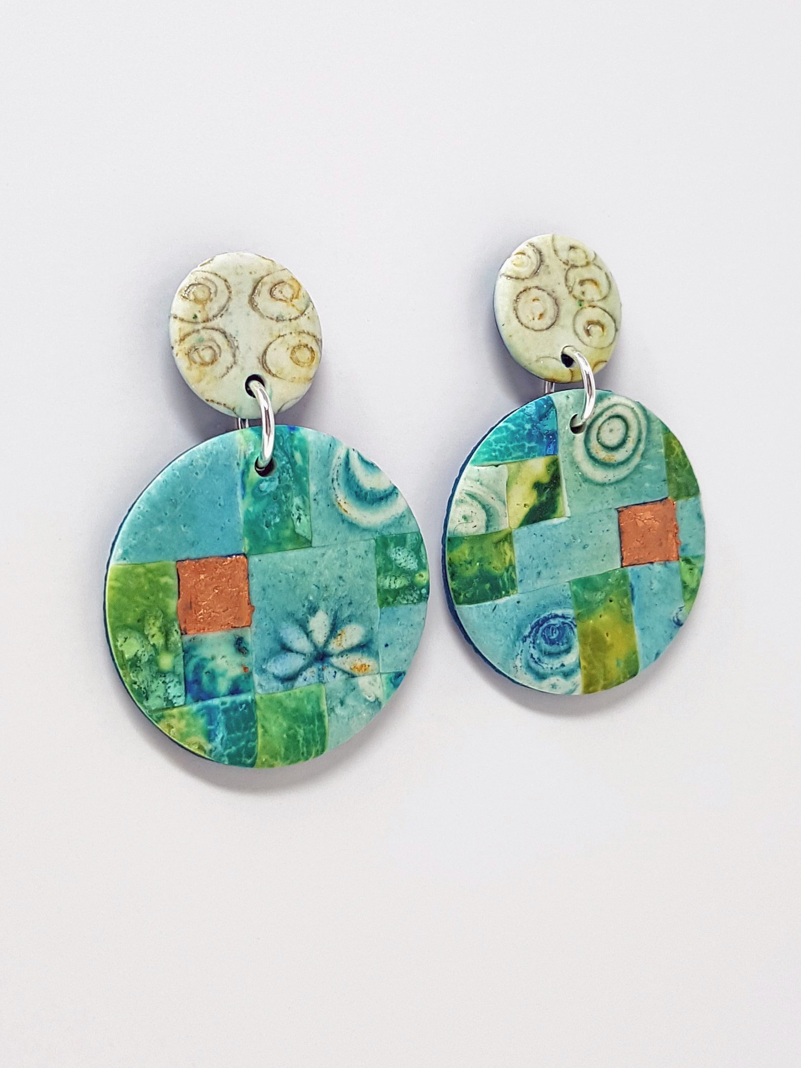 Stud earrings with cream top bead stamped gold circular pattern; the bottoms are turquoise, teal, blue flower, water patterns with bronze accent tiles.