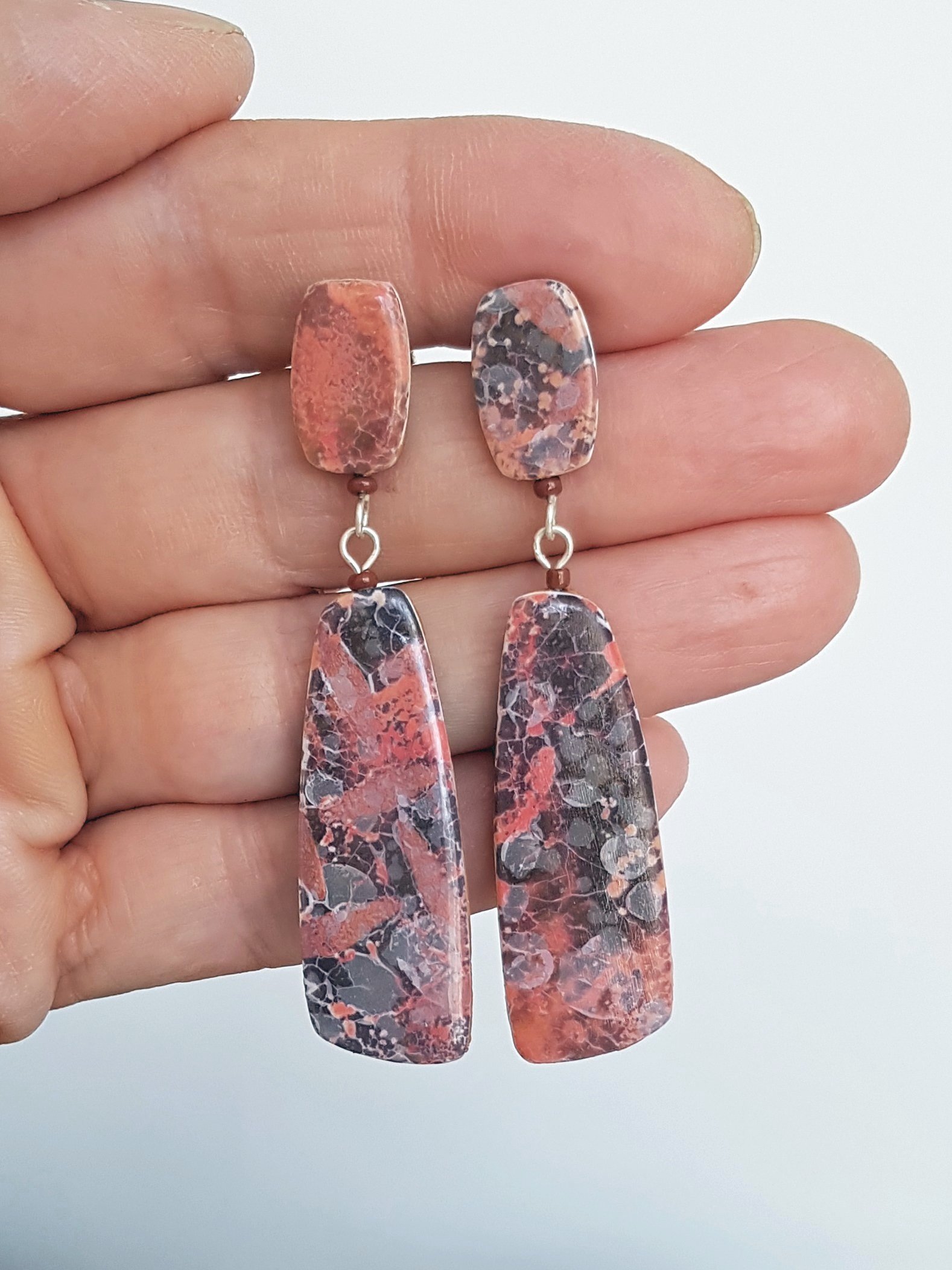 Slate grey and pinky red dangle earrings with stud tops held between fingers.