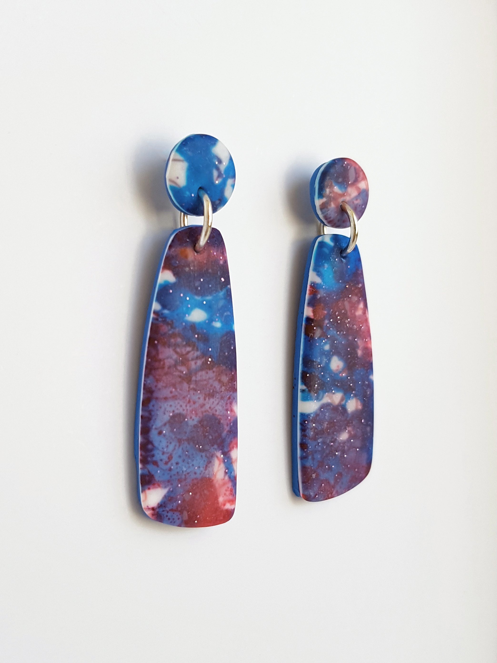 Blue, red and white mismatched dangle earrings with a matte, line and brushstroke pattern and subtle glitter elements catching the light.
