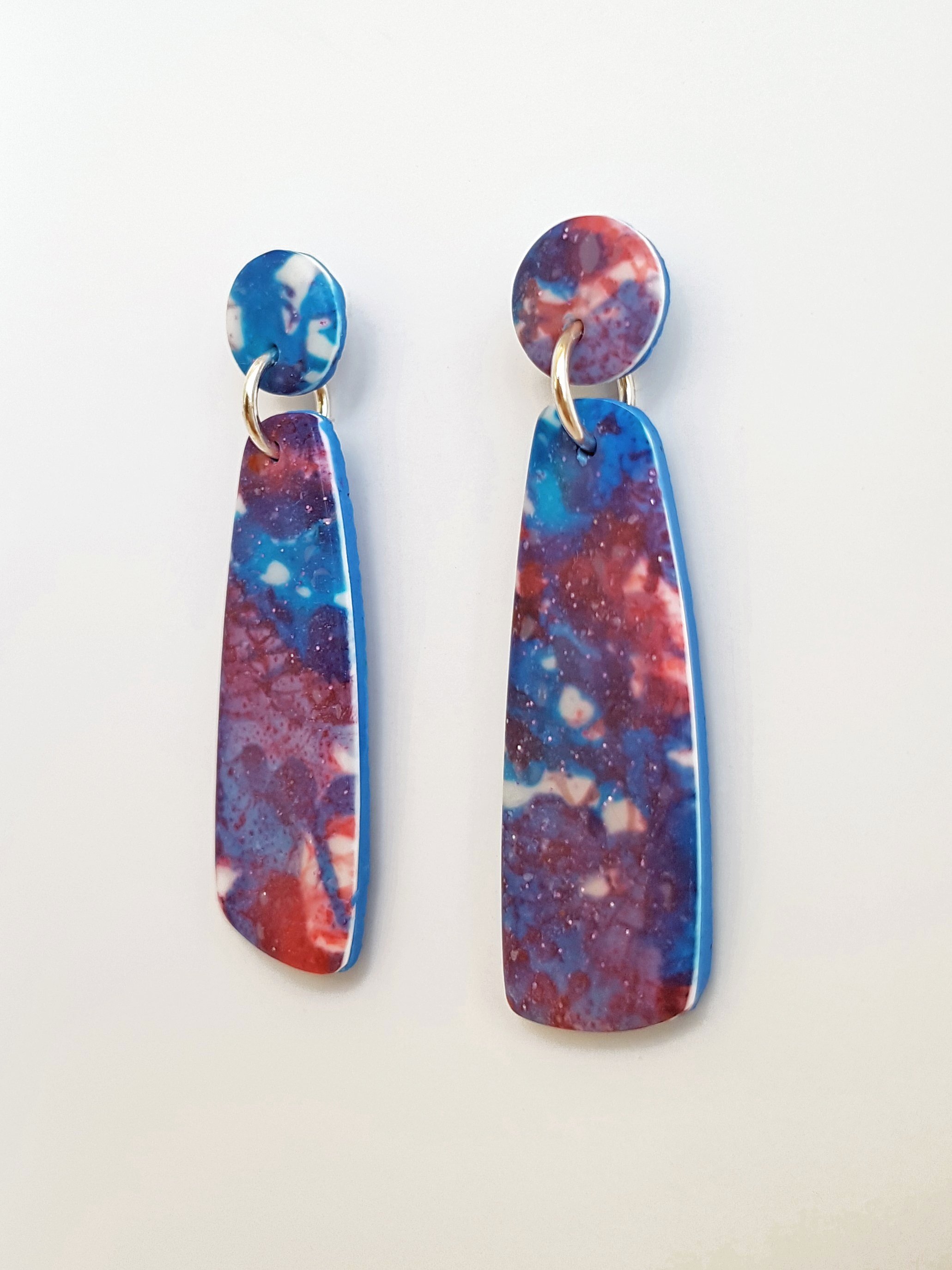 Flat profile blue, red and white mismatched dangle earrings with a matte, line and brushstroke pattern and subtle glitter elements catching the light.