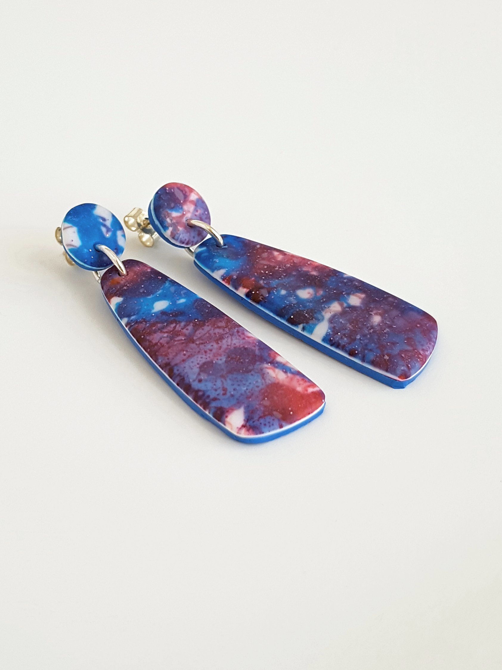 Blue and white edge profile of blue, red and white mismatched dangle earrings with a matte, line and brushstroke pattern.