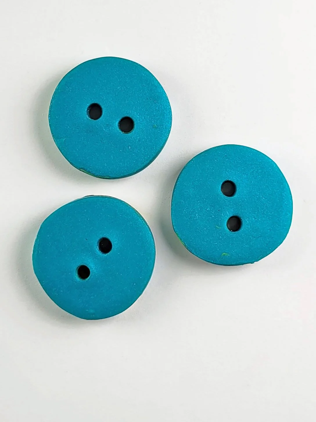 Three buttons pictured from above, lying on their faces, against a white background, to show their backs