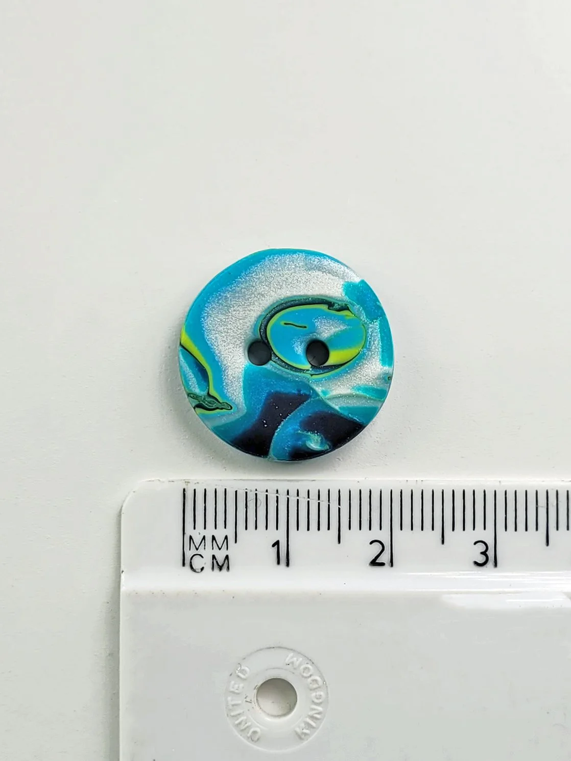 A single buttons lying against a ruler to show its 20 mm (9/16 inch) diameter