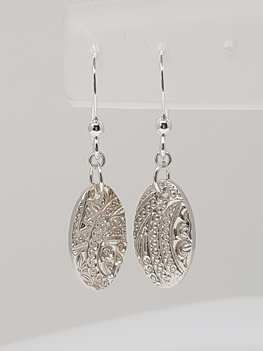 A pair of fine silver oval dangle earrings embossed with a paisley pattern.