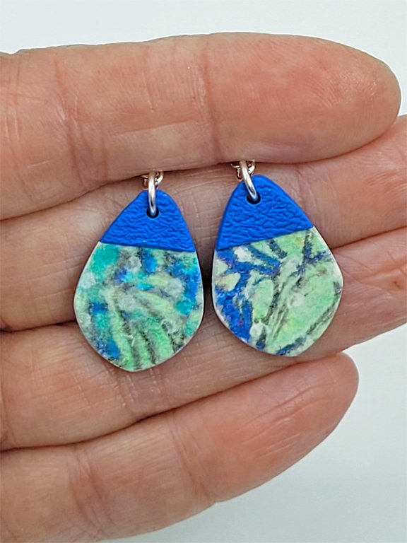 Wide teardrop Sprig Blue Tip Earrings held in a hand to demonstrate their size and intricate craftsmanship.