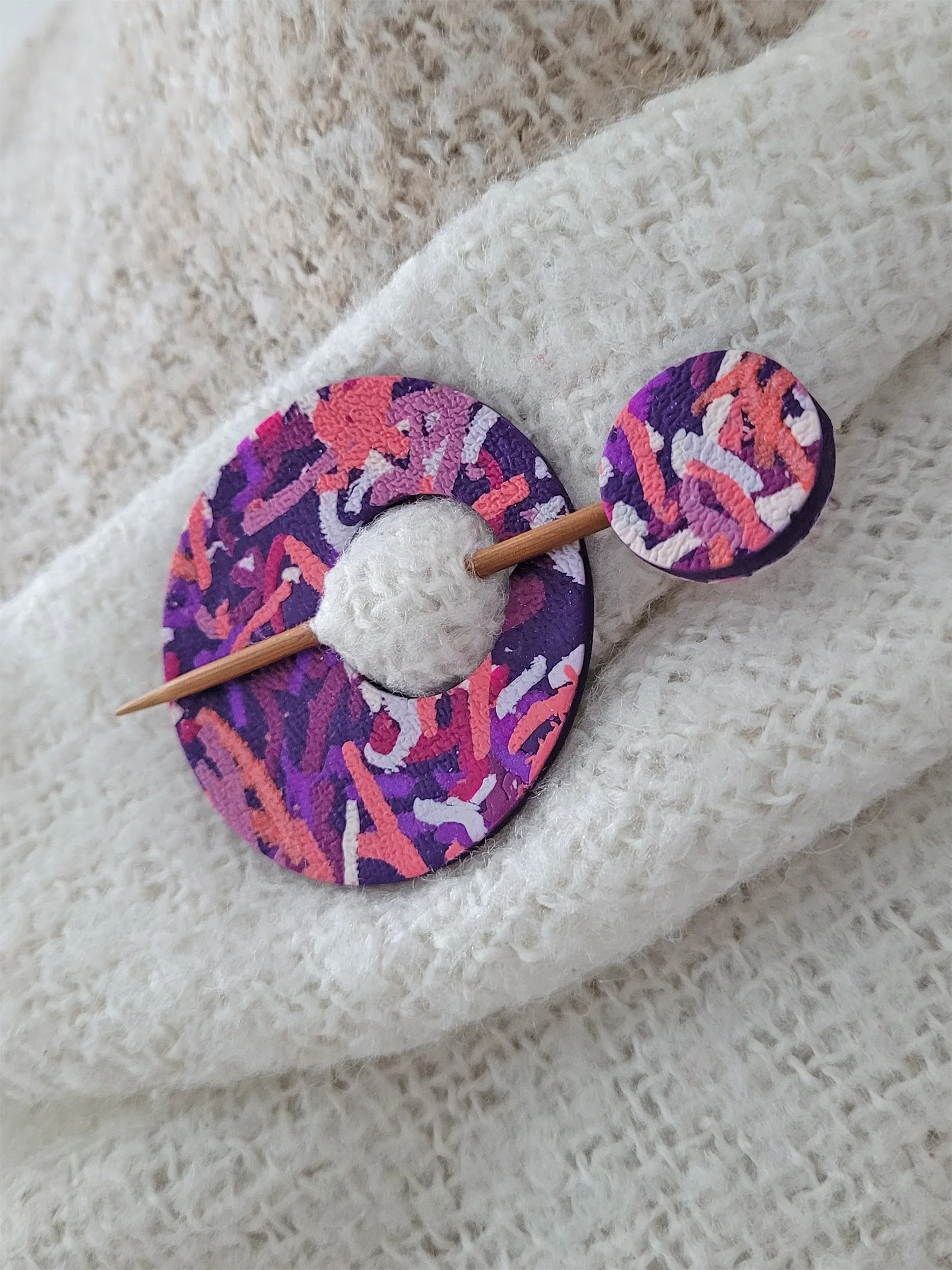 Purple Ticker Tape circular Pin shown from the right edge, pinned to a cream shawl.