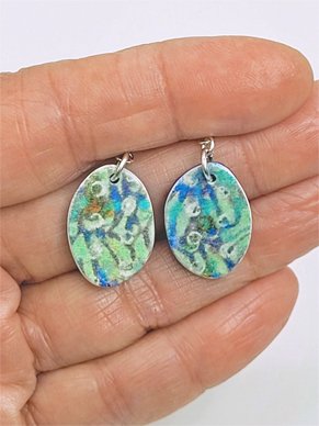 A pair of oval dangle earrings held in a hand, showing their size and pattern on the surface.
