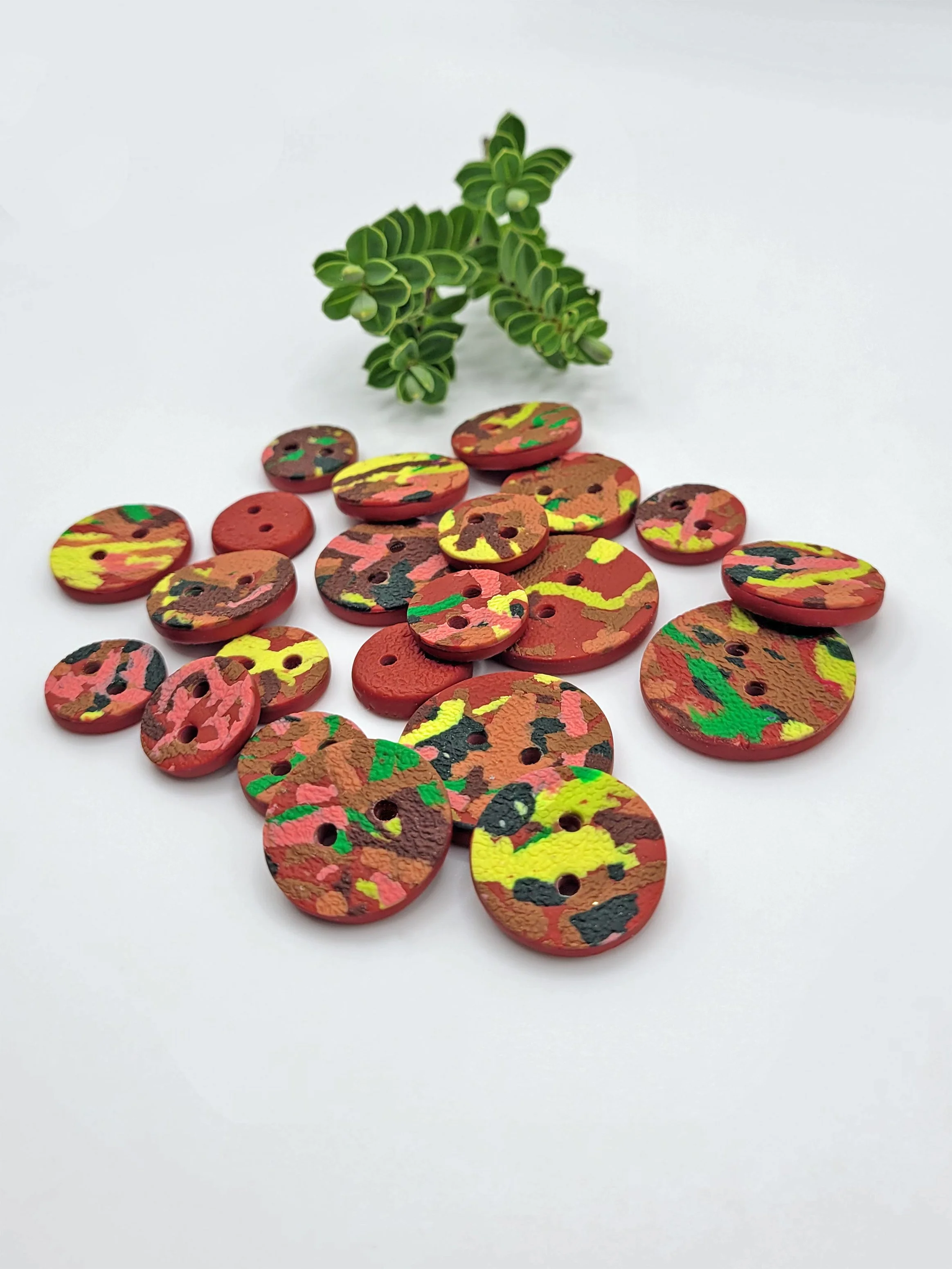Terracotta Ticker Tape buttons scattered on a white surface with a small green plant the background