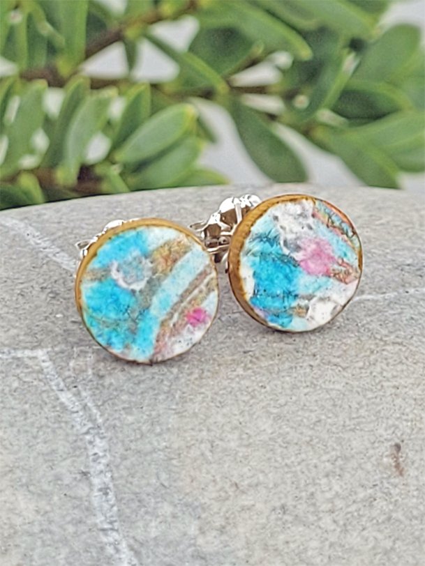 Turquoise, pink, white and ginger brown stud earrings balanced on a pebble highlighting their artisan aesthetic.