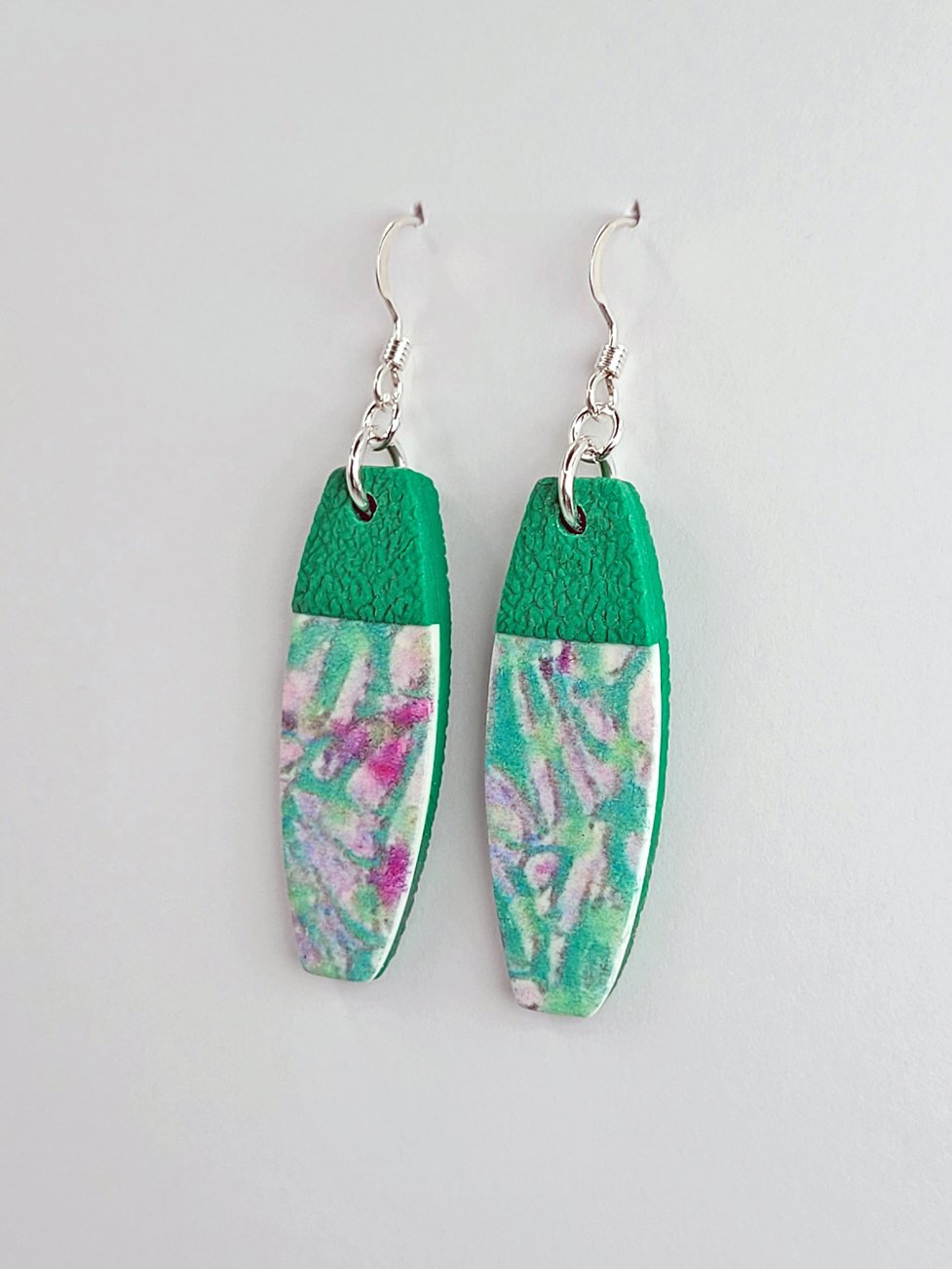 Close-up of tablet earrings showing their smooth floral front and textured green polymer clay tops and backs for contrast.