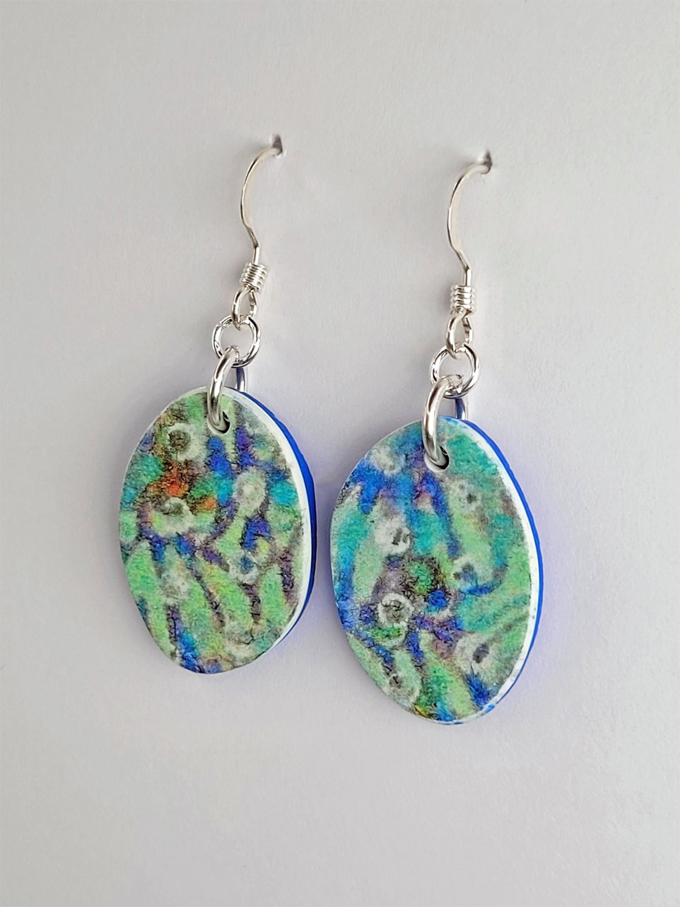 Close-up of flat oval dangle earrings showing their smooth floral fronts.