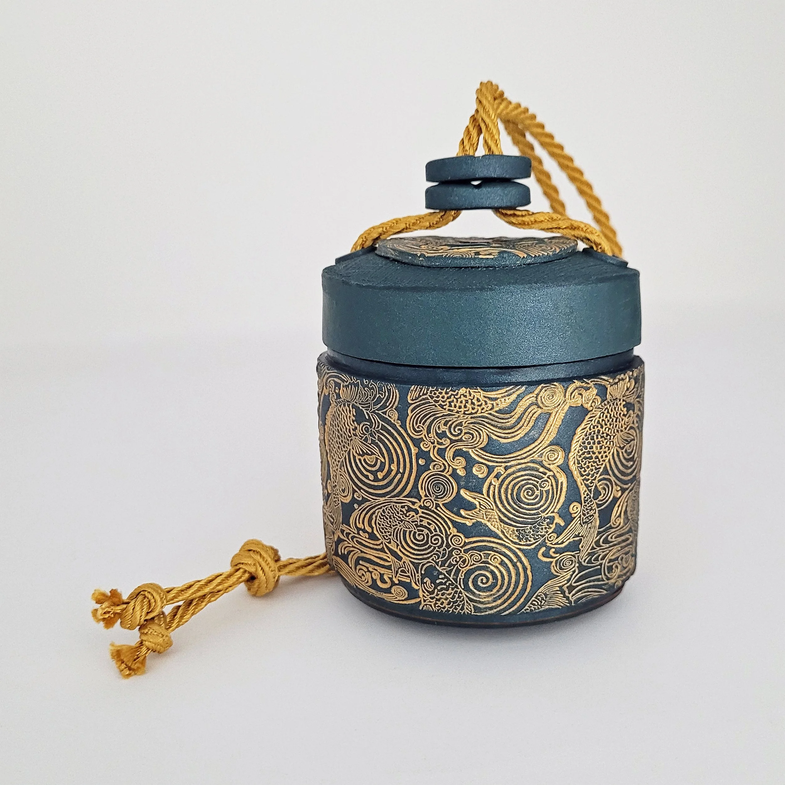 A round, green lidded box with a gold cord, embossed and decorated in gold with swimming koi carp