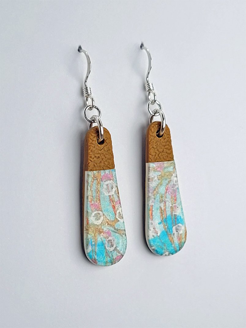 Side view of teardrop earrings with patterned upper layer with pastel floral pattern and smooth finish, contrasting with the textured ginger tone tips and backs.