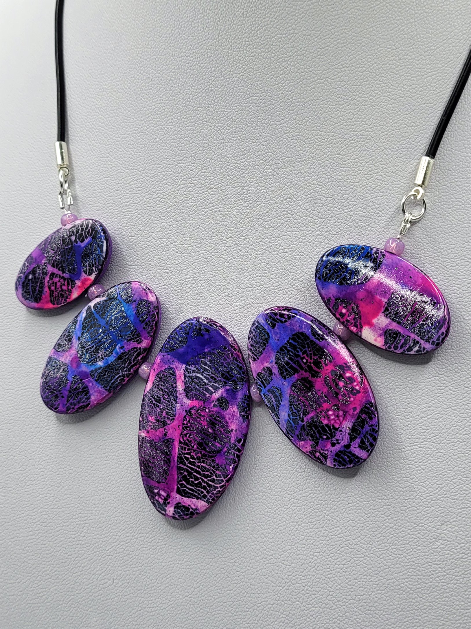 The larger middle bead has two smaller neighbours on each side decreasing in size. They are strung on a round, faux rubber cord.