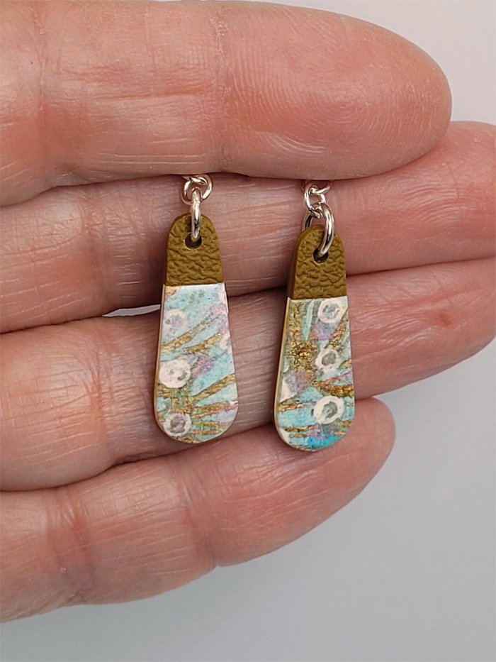 Delicate floral and ginger teardrop earrings held in a hand to illustrate their size and design details.