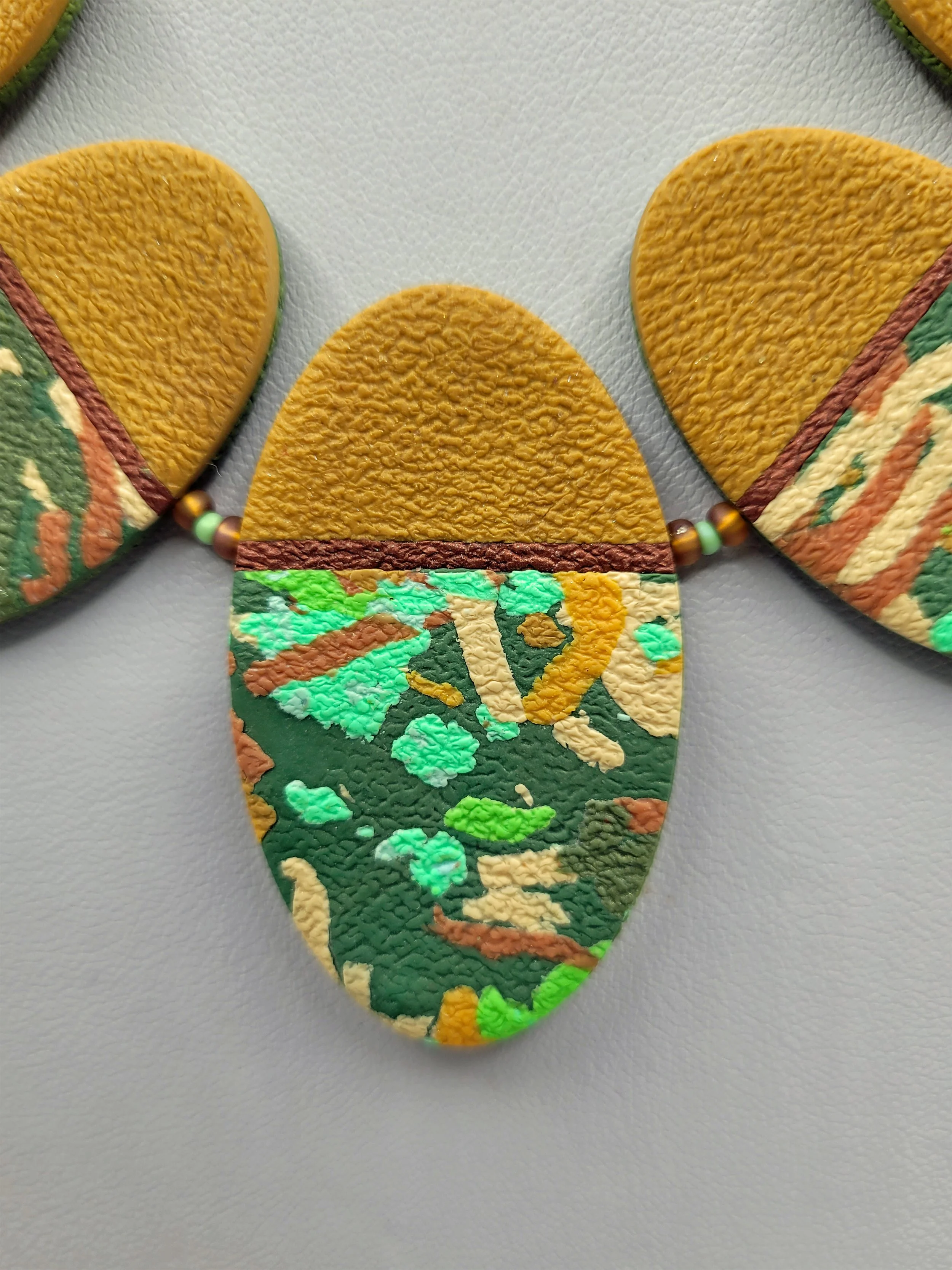 A close up of the mustard, olive, green and pale blue centre bead showing a detail of the intricate pattern and texture.