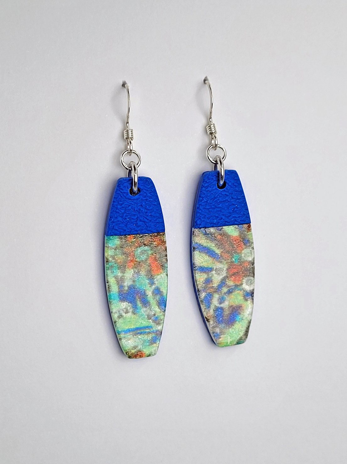 Side view of long rectangular earrings emphasizing their pastel floral pattern and smooth, satin finish, contrasting with the textured blue upper portion.