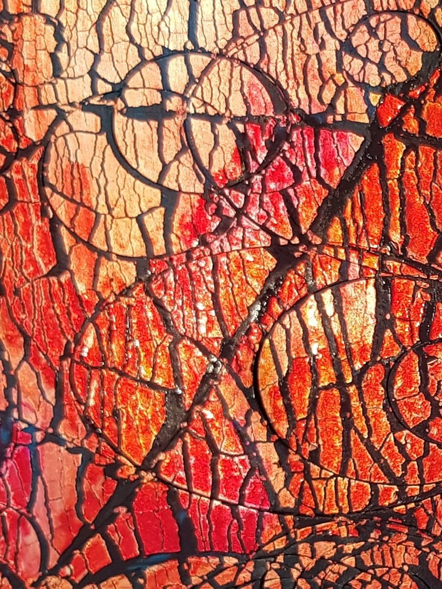 close up of orange, red and gold alcohol inks on crackled black clay.