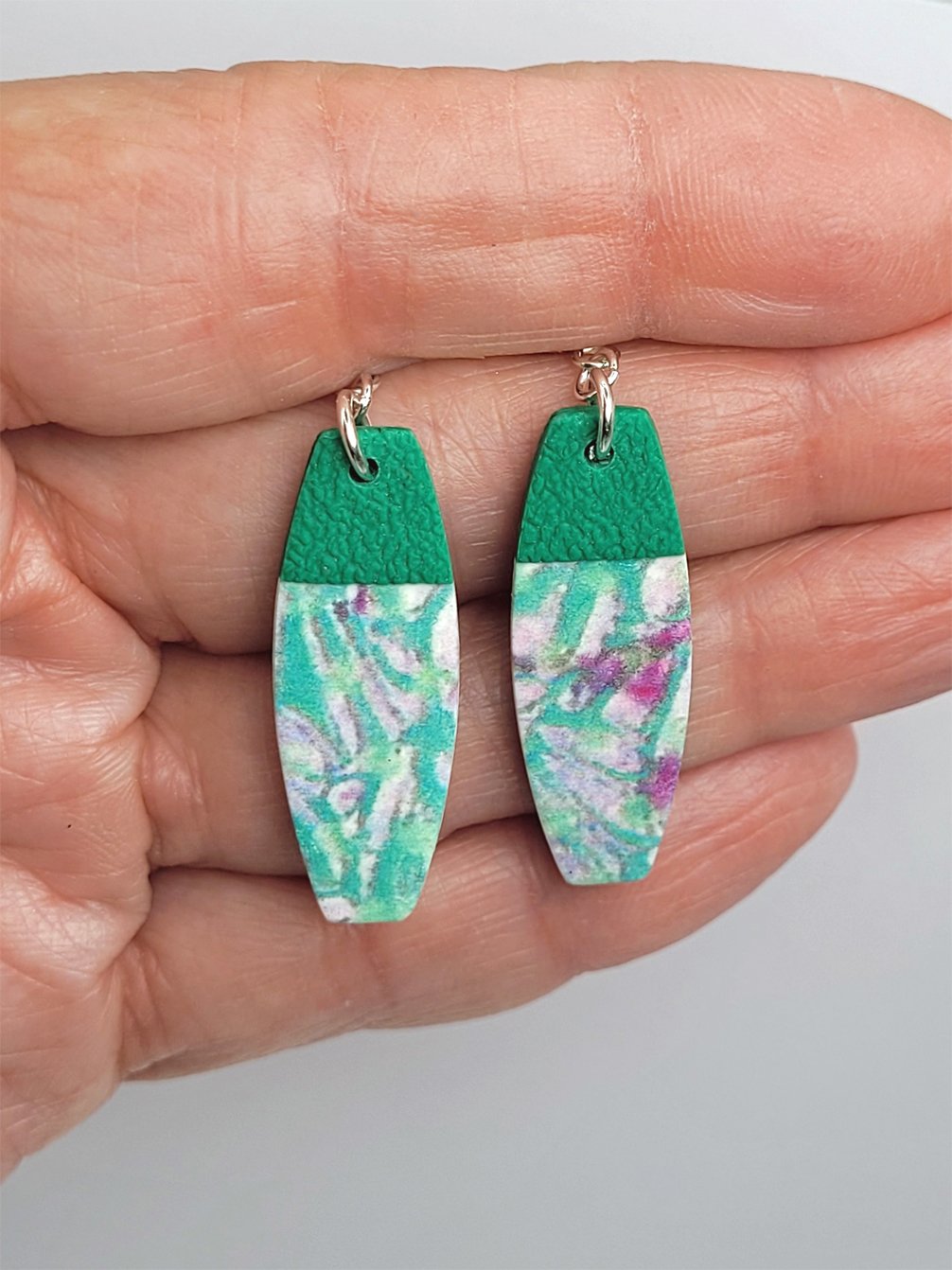 Convex rectangular earrings held in a hand, showing their size and intricate surface detailing.