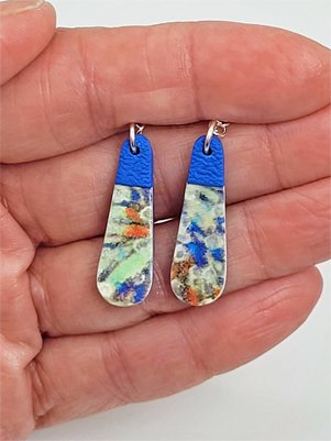Blue and green flat teardrop earrings held in a hand, illustrating their size and intricate pattern detailing.
