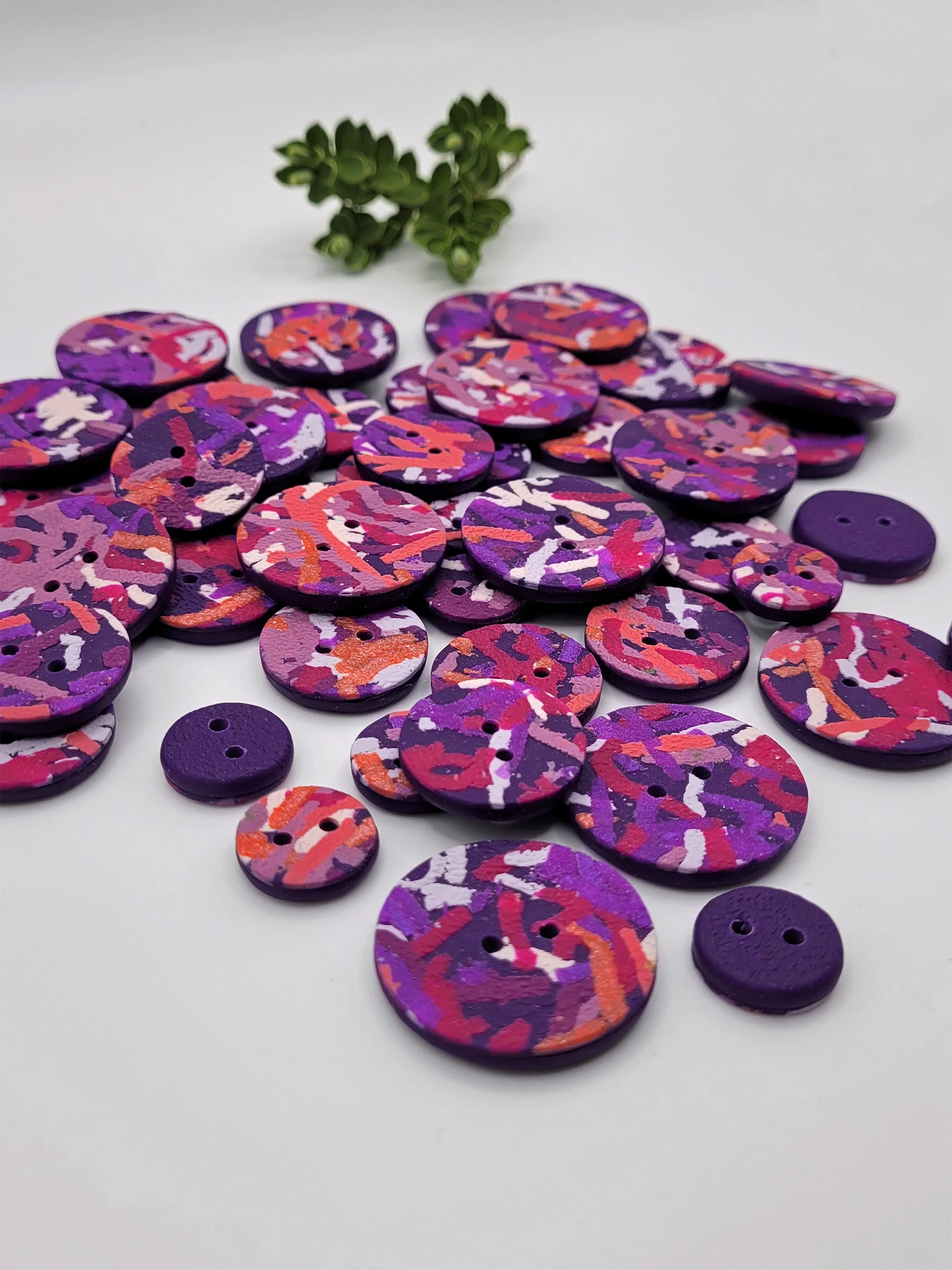 Mixed sizes of Purple Ticker Tape buttons, some with their purple backs showing.