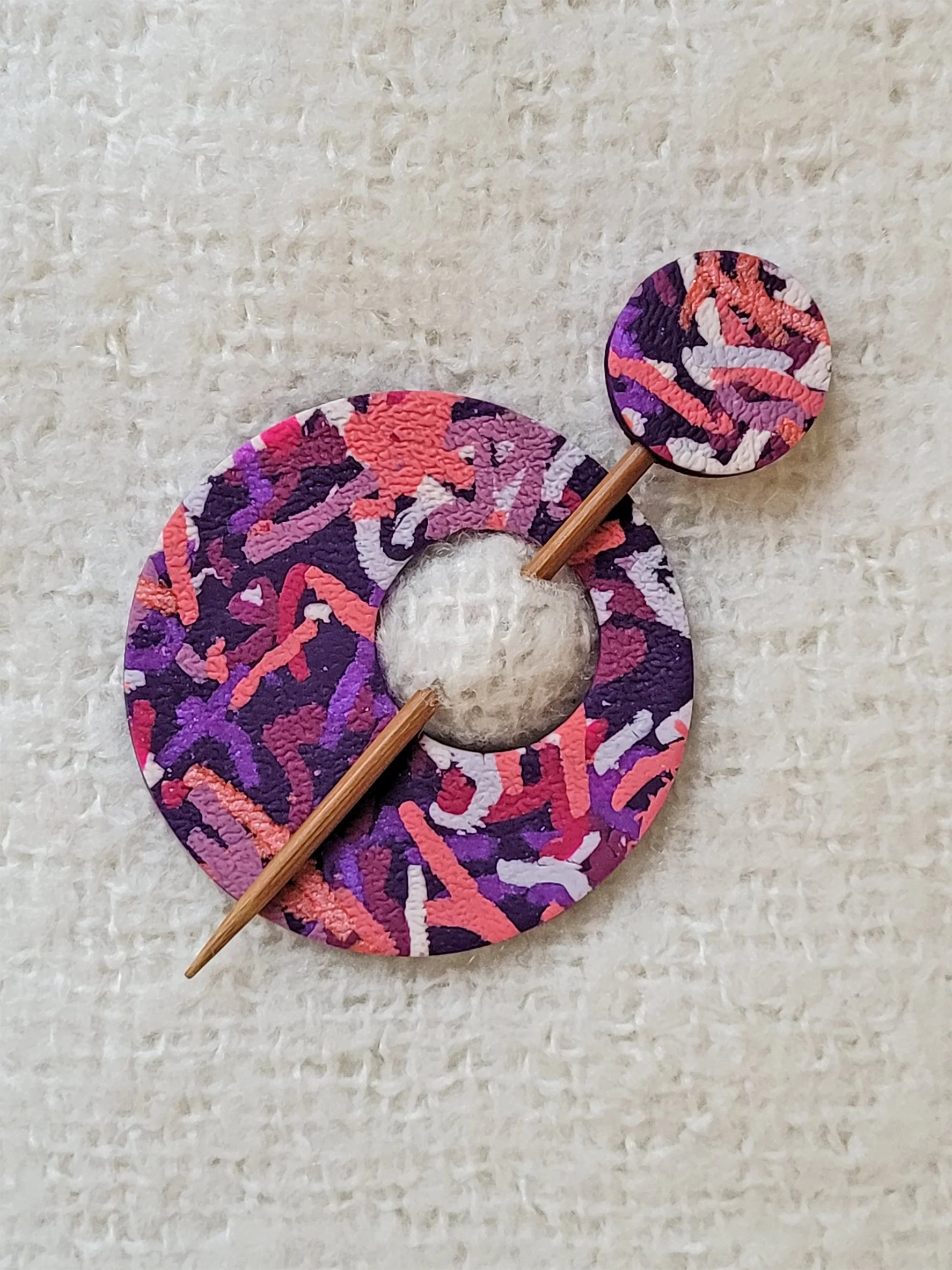 Flat lay image of Purple Ticker Tapepolymer clay shawl pin, with a bamboo pin, topped with a matching round disc.