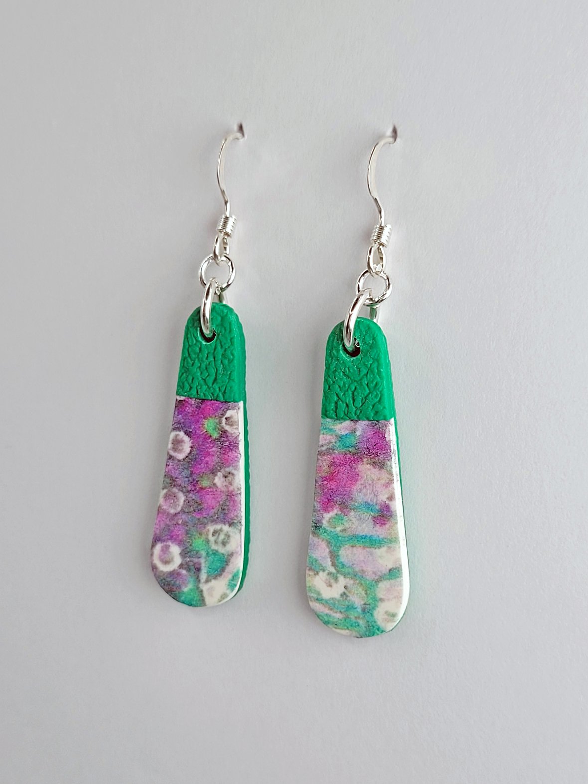 Close-up of pink, mauve and green teardrop earrings showing their smooth floral front and textured clay back with sterling silver earwires.