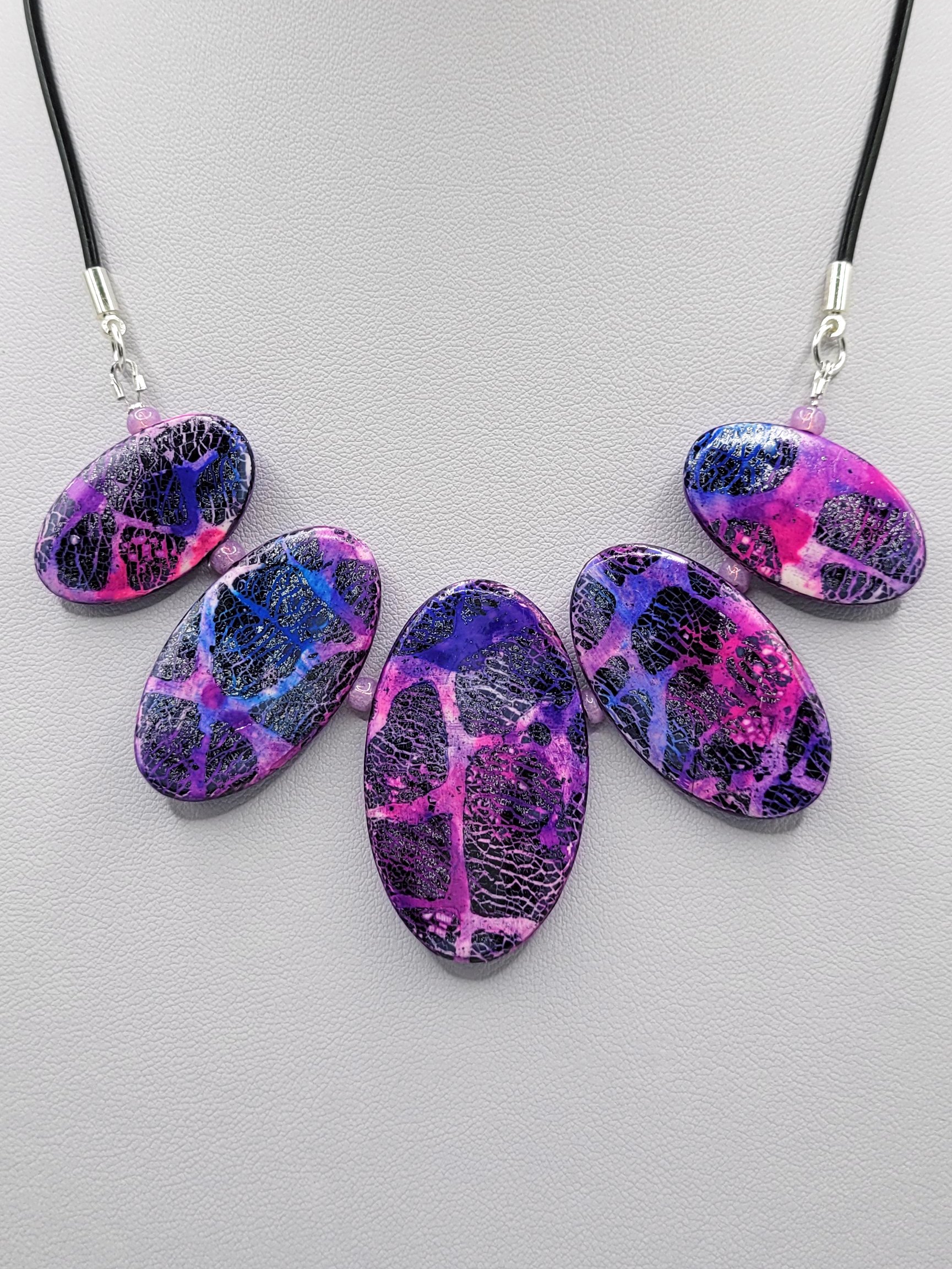 Statement necklace with 5 flat, pink, purple, blue, white and black oval beads which get larger in the middle.
