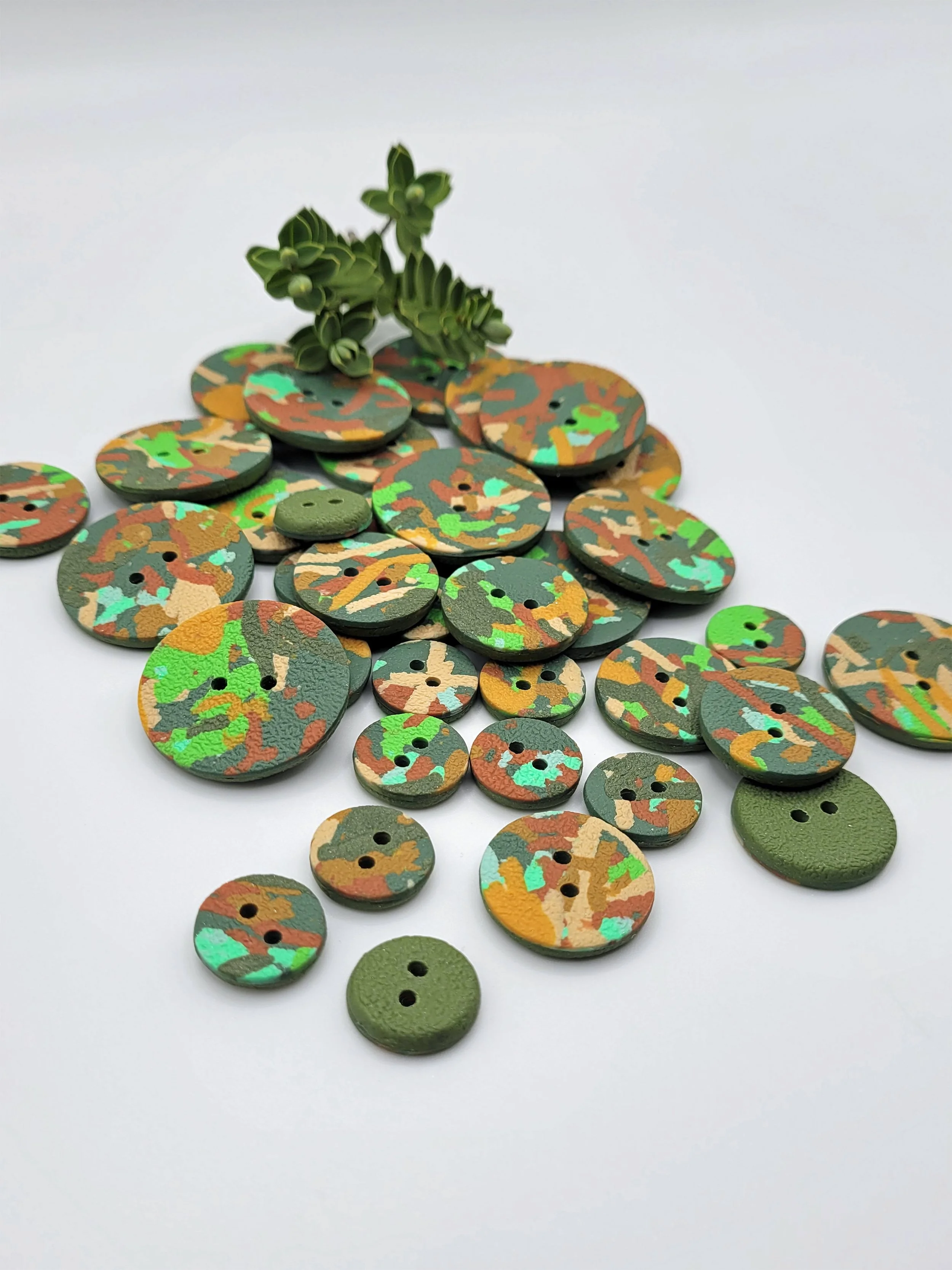 Mixed sizes of Green Ticker Tape buttons, some with their olive green backs showing.