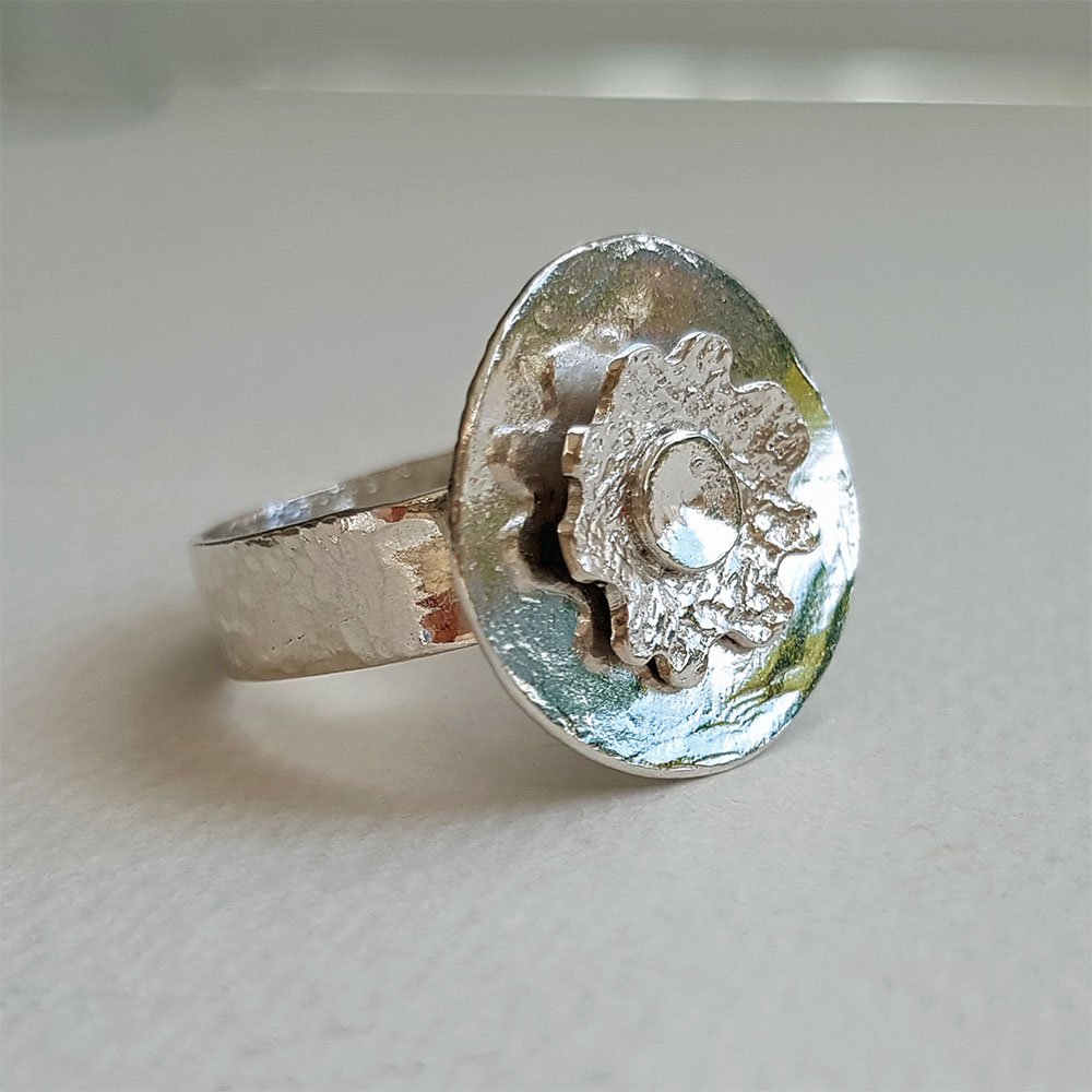 A flower is layered on top of a highly polished round disc adding dimension to a silver ring.