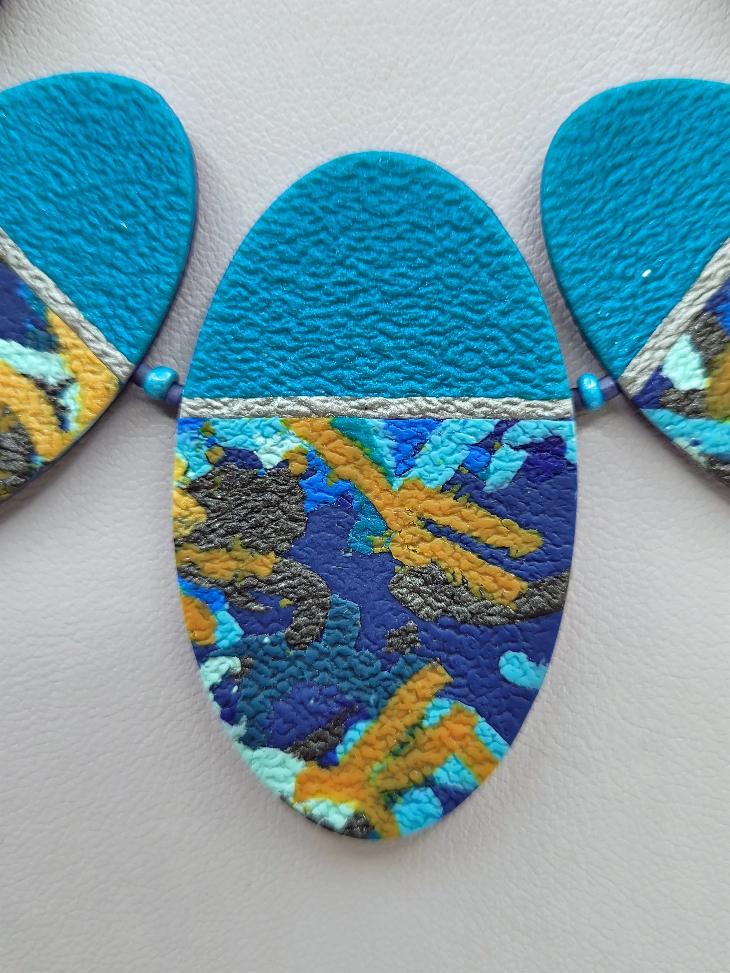 A close up of the blue, turquoise, grey and orange centre bead showing a detail of the intricate pattern and texture.