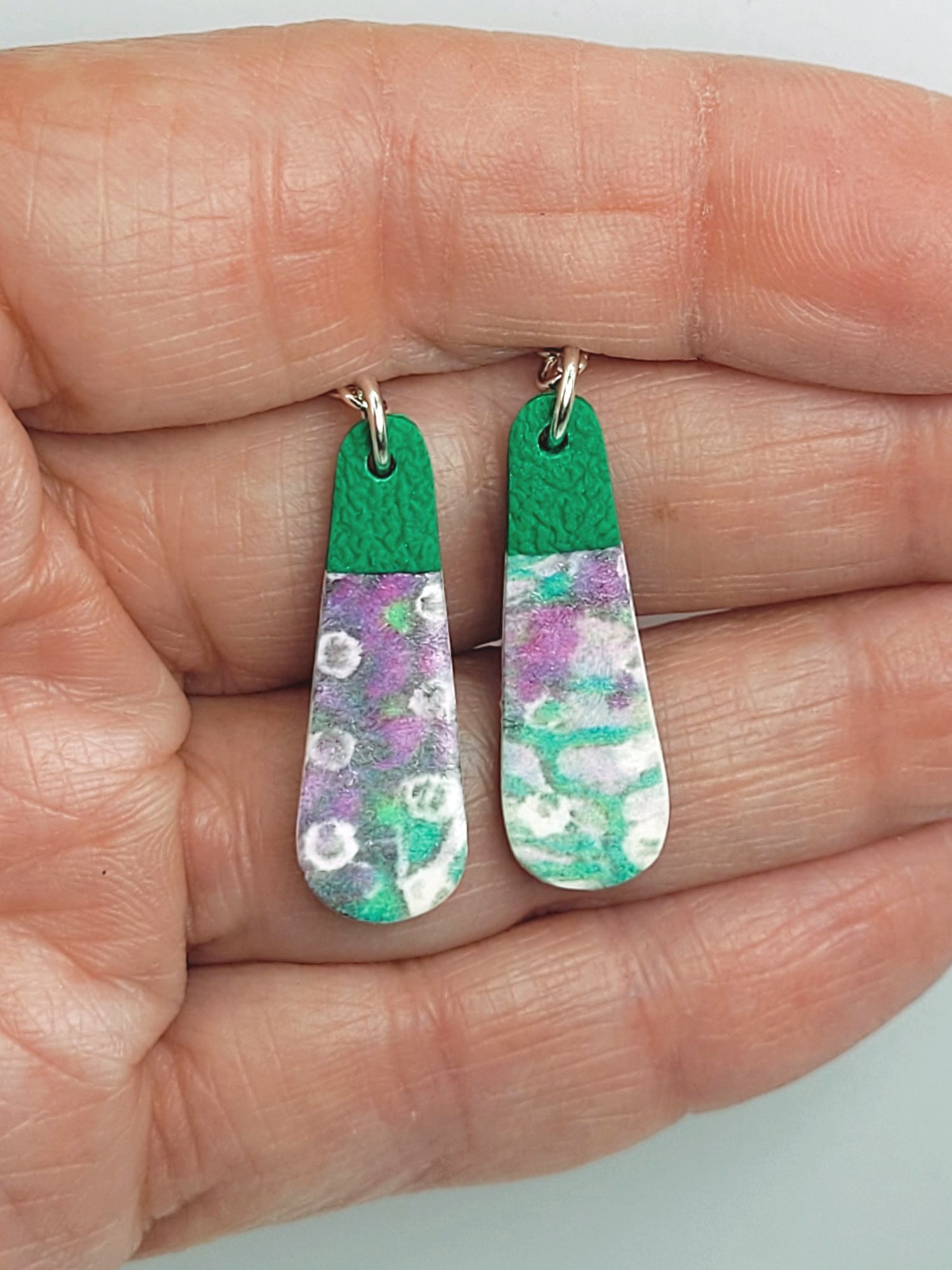 Classic teardrop earrings held in a hand, illustrating their size and intricate pattern detailing.