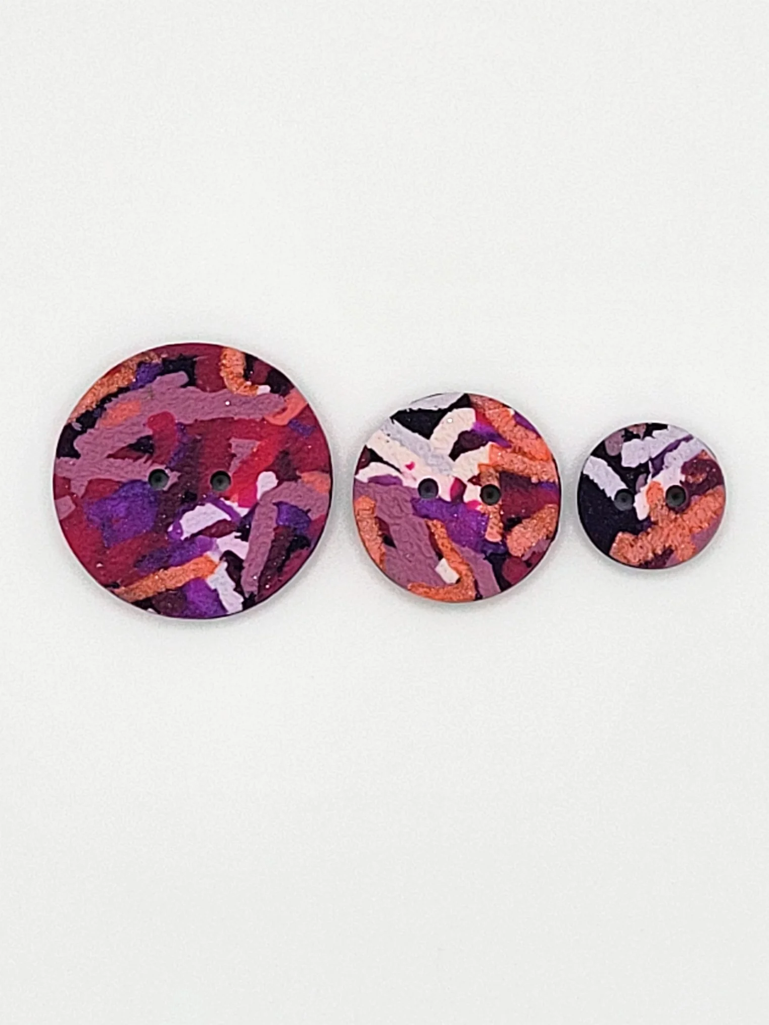 Flat lay of Purple Ticker Tape buttons in 3 different sizes.