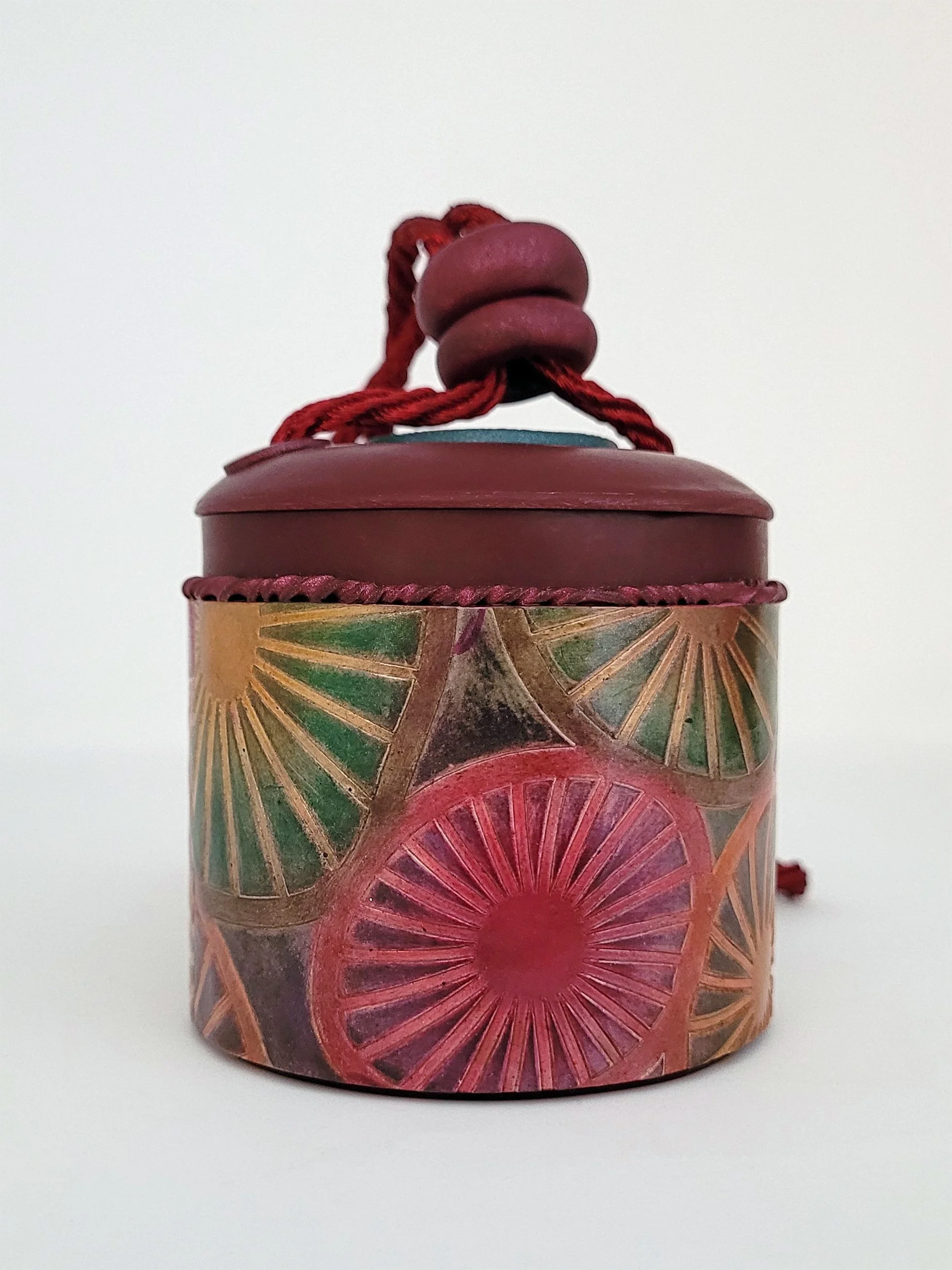 A round burgundy lidded box with a circular surface pattern