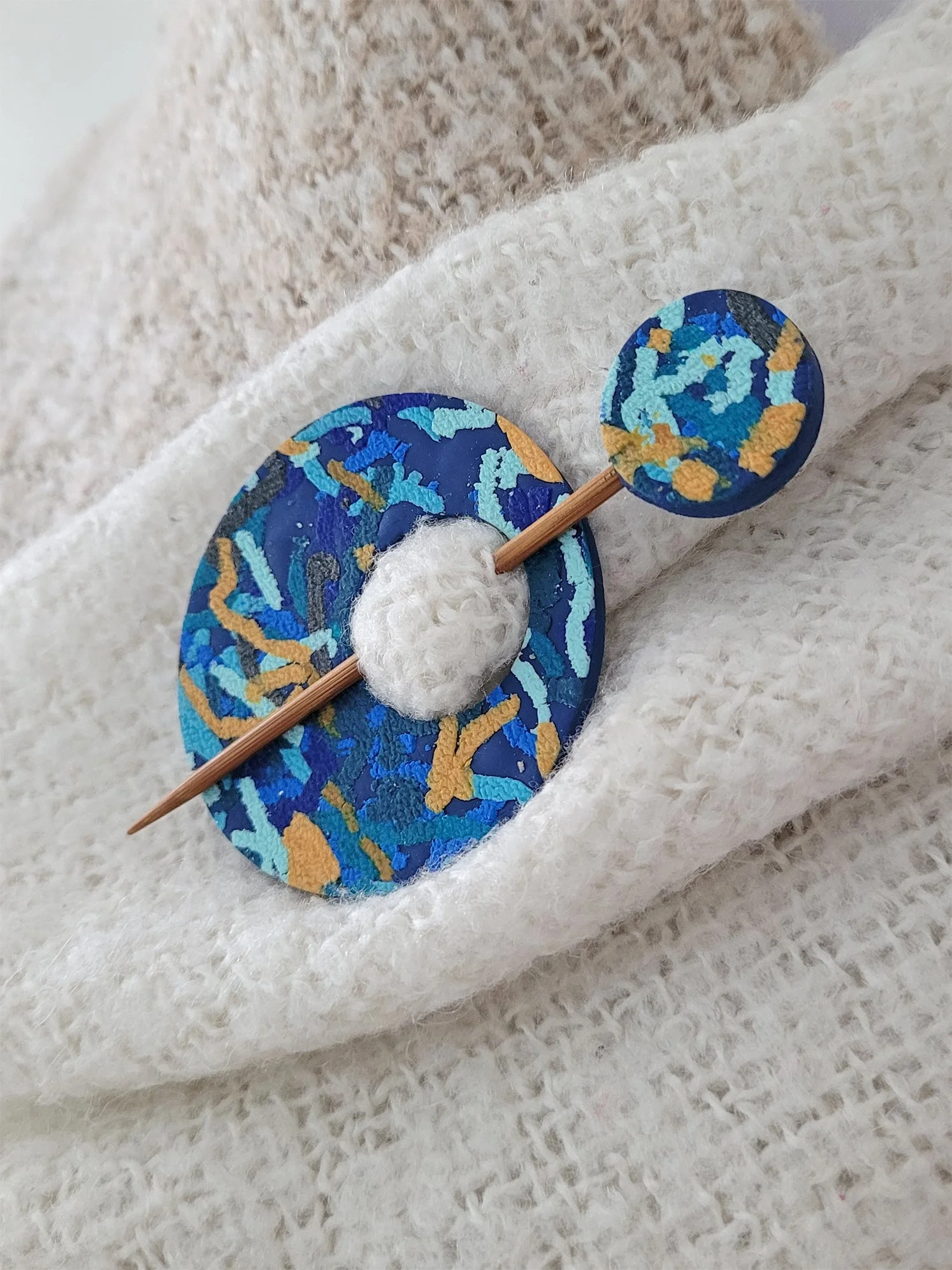 Circular disc style Blue Ticker Tape Pinshown from the right edge, pinned to a cream shawl.