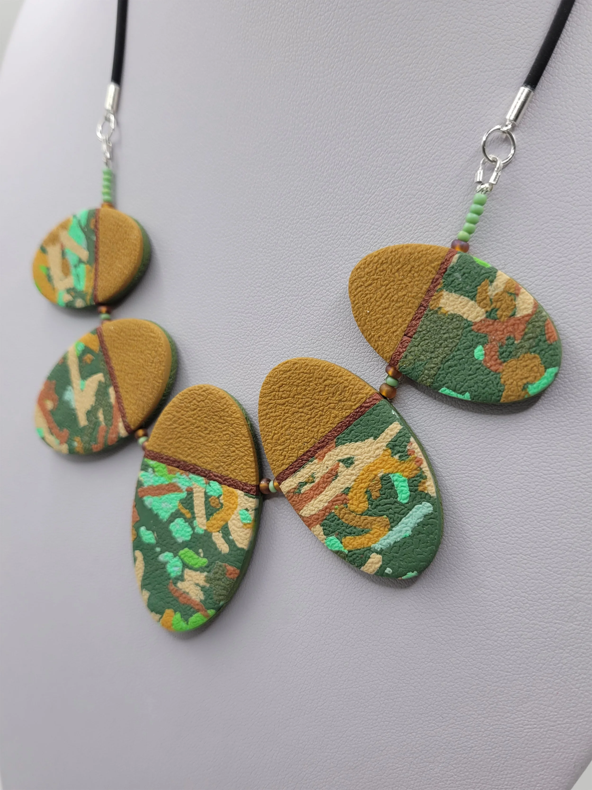 Each oval bead features an ochre yellow upper third separated by a thin bronze band from the lower two thirds of abstract ticker tape style pattern.