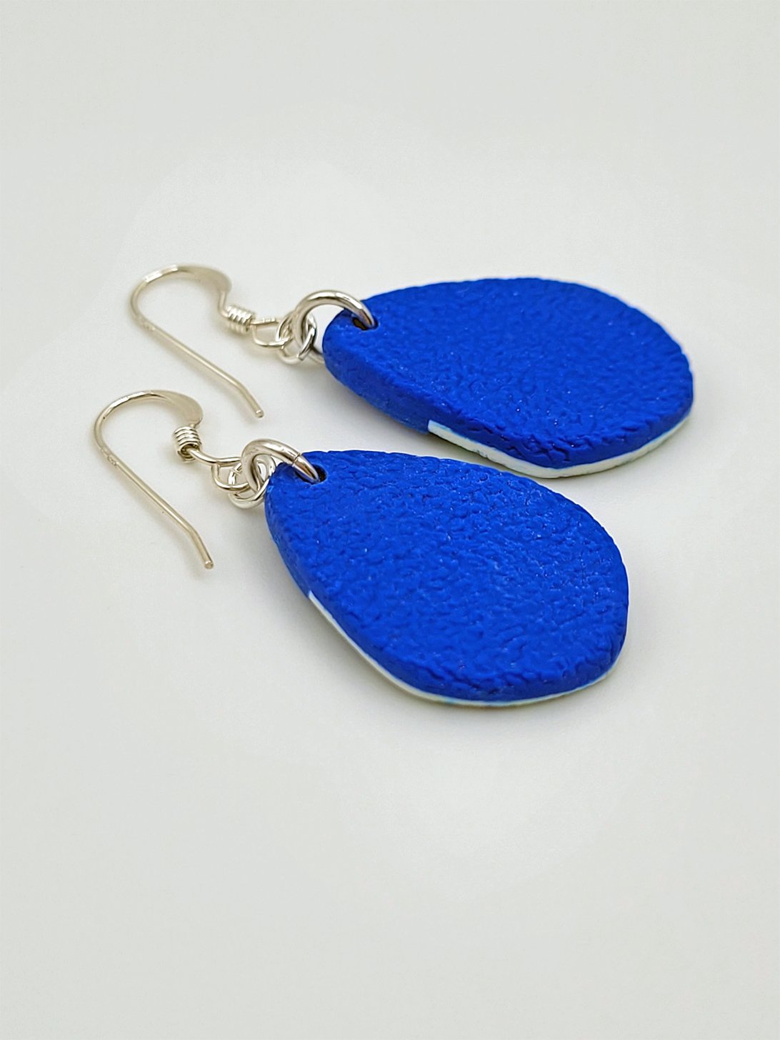 Back view of rounded-tip 'fat' teardrop earrings in textured bright blue polymer clay with sterling silver earwires.