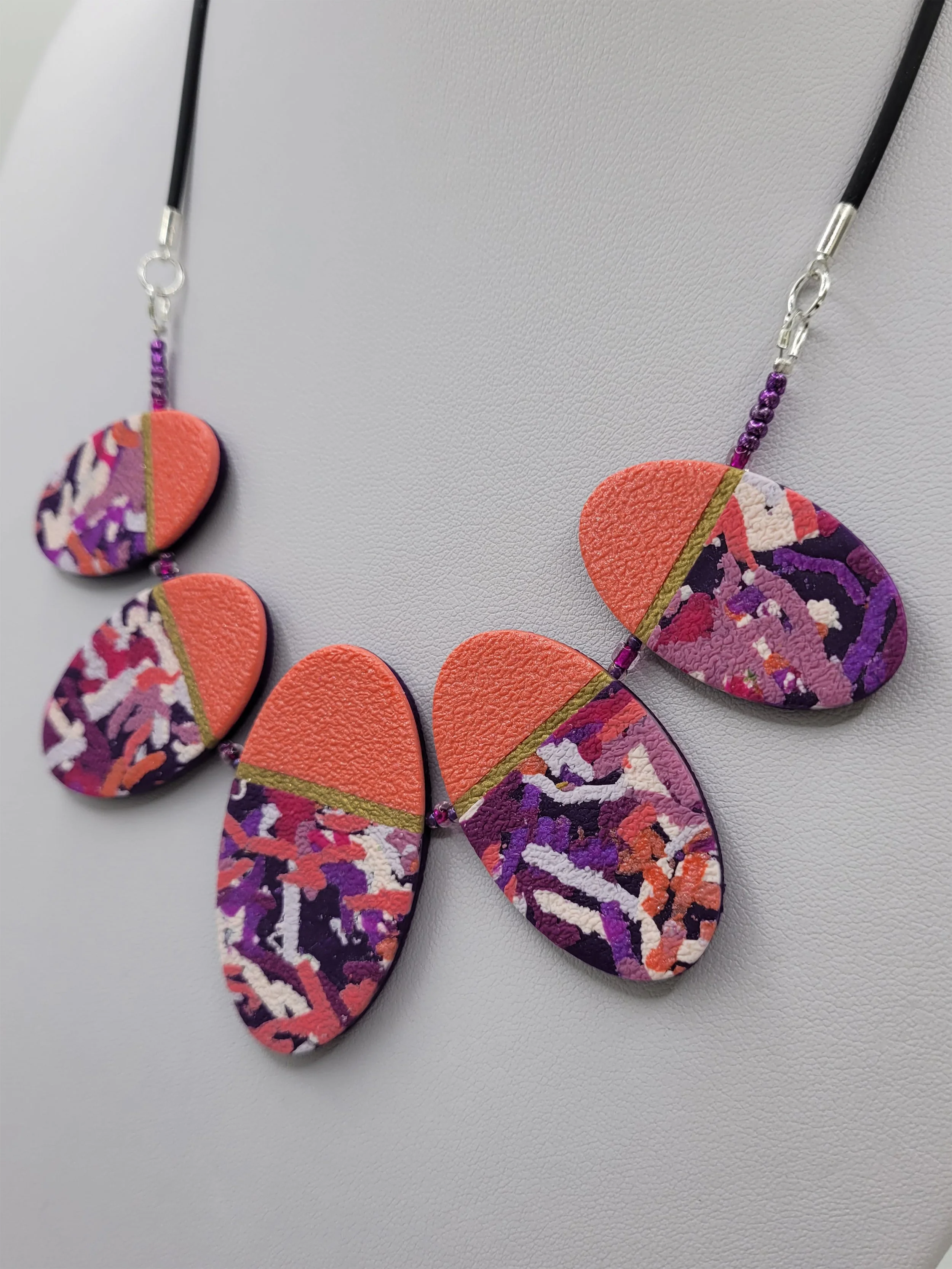 Each oval bead features a pearlescent salmon pink upper third separated by a thin antique gold band from the lower two thirds of abstract ticker tape style pattern.