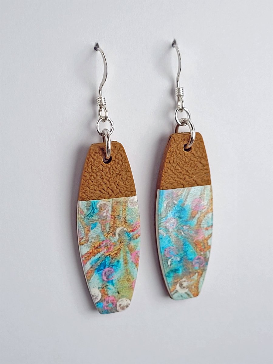 Side view of long rectangular earrings emphasizing their unusual shape and pastel floral pattern. Their smooth, satin finish contrasts with the textured ginger upper portion.