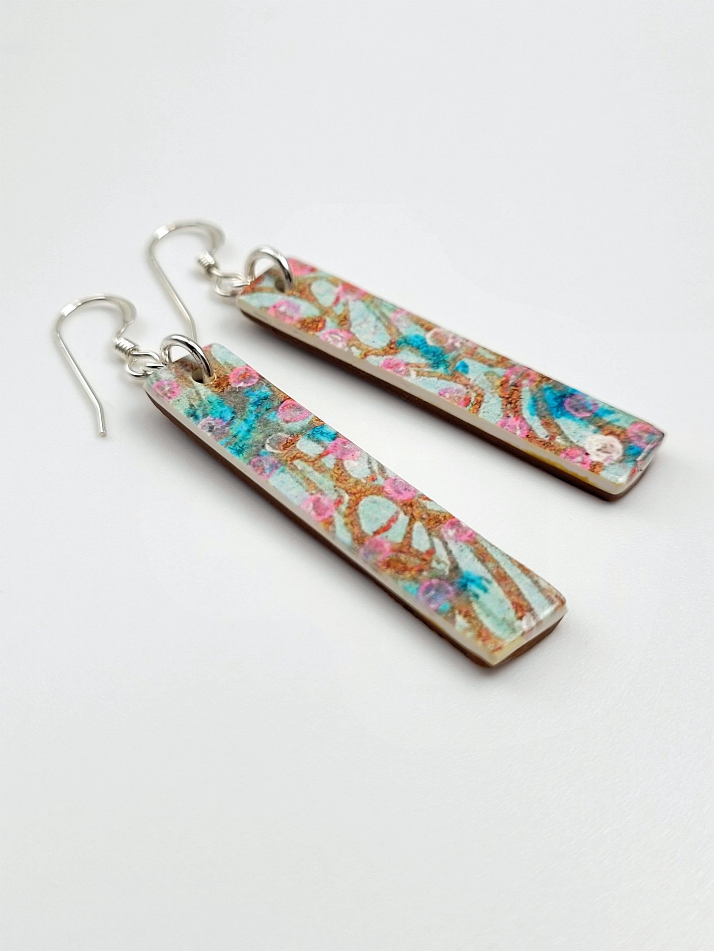 Flat lay of Sprig Ginger Cane earrings highlighting their contemporary pastel floral design and long, elegant shape.