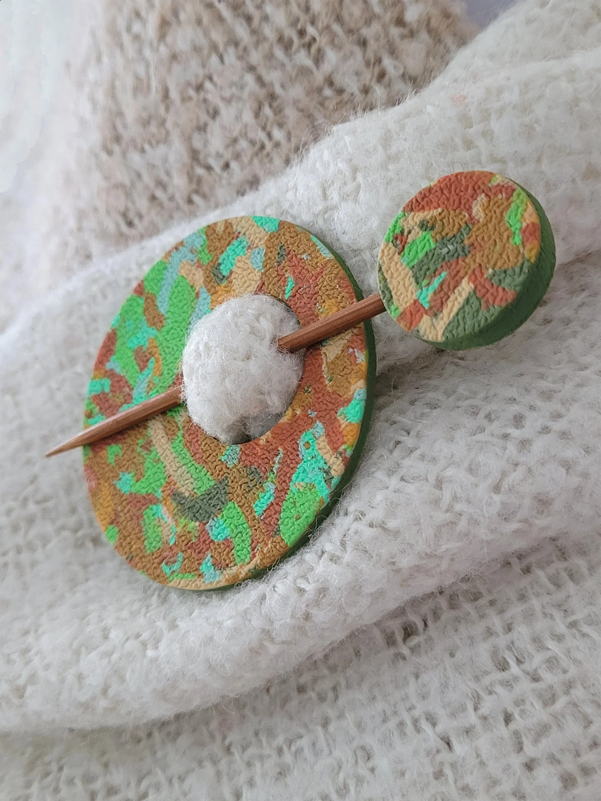 Green Ticker Tape circular Pin shown from the right edge, pinned to a cream shawl.