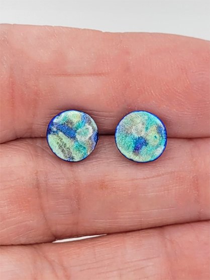 Sprig Blue Studs held between fingers to highlight their size.