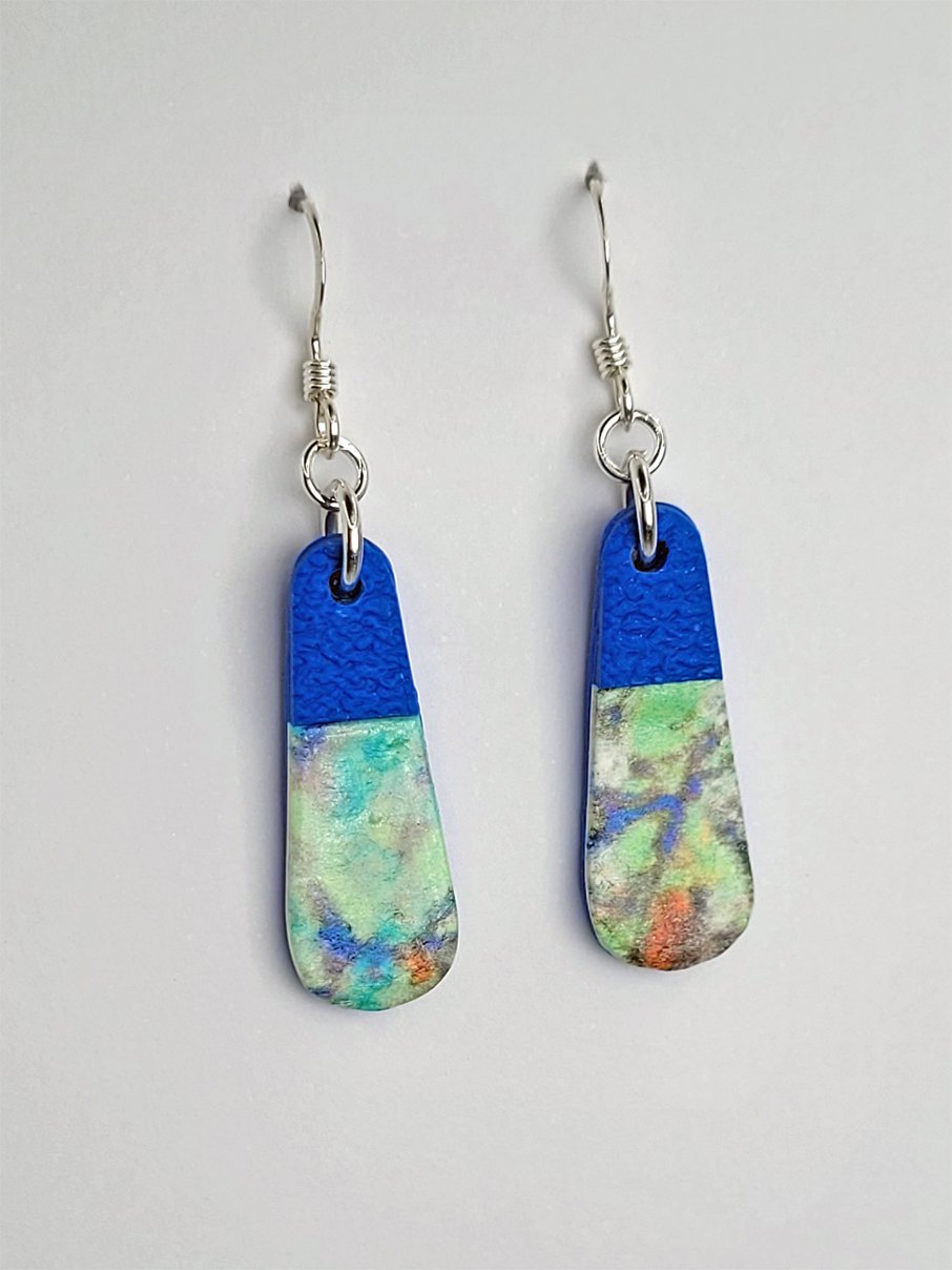 Side view of droplet-shaped earrings showing the soft abstract floral pattern with satin finish and contrasting matte cobalt blue accents.
