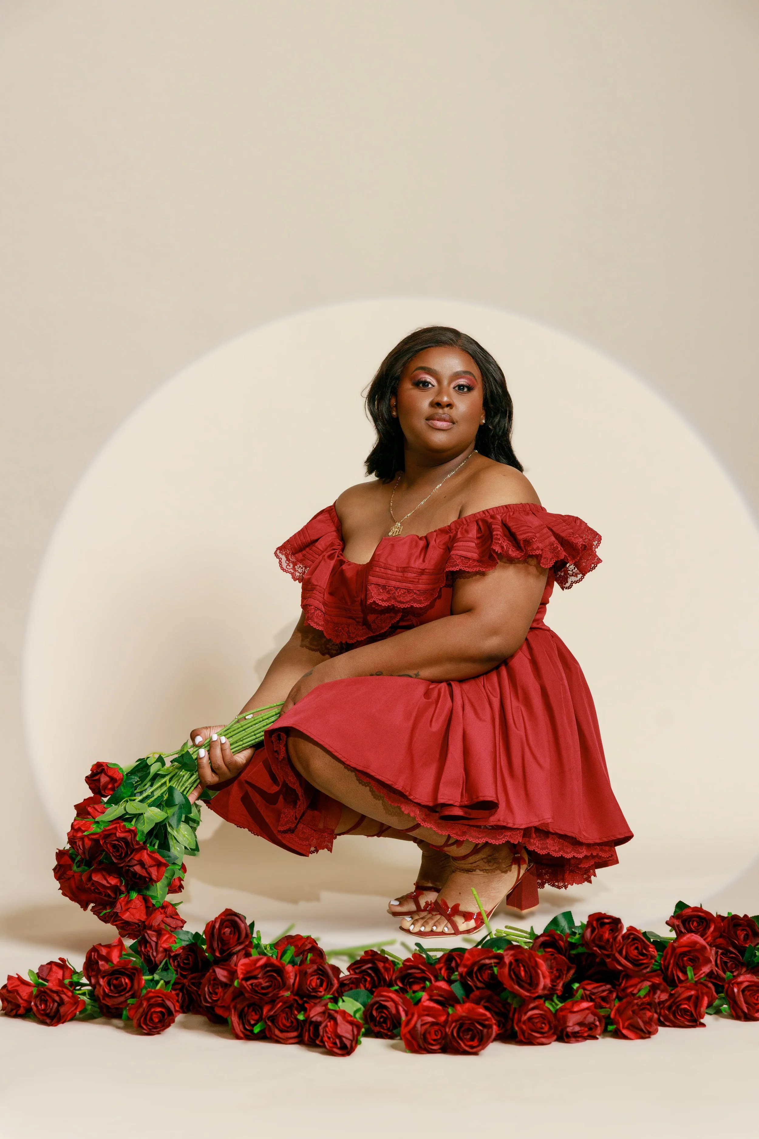 A woman in a red dress and red high heel shoes is holding a bouquet of red roses, surrounded by a large collection of roses on the floor, in front of a white background with a circular cutout.