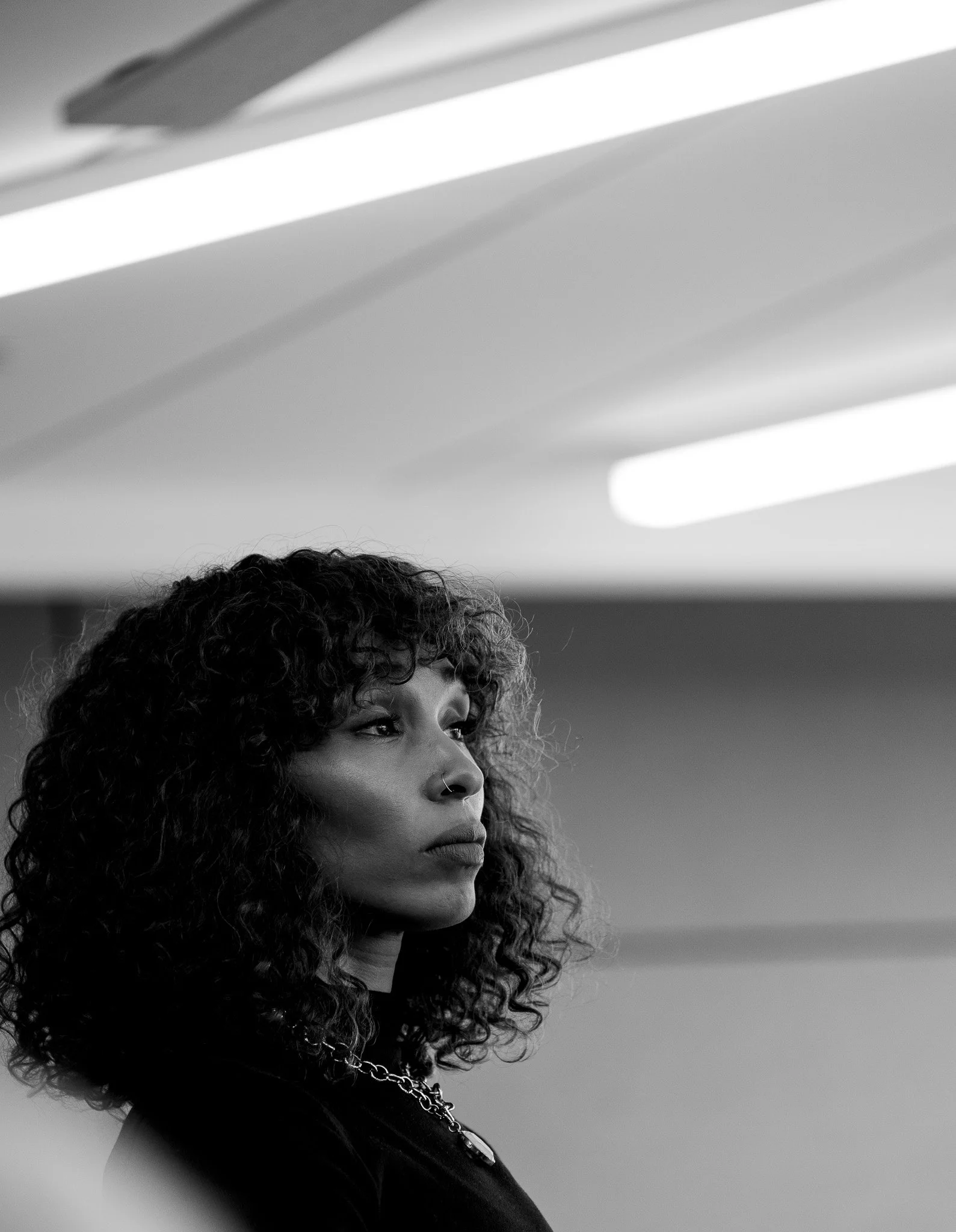 A woman in profile beneath fluorescent light, her gaze fixed beyond the frame.