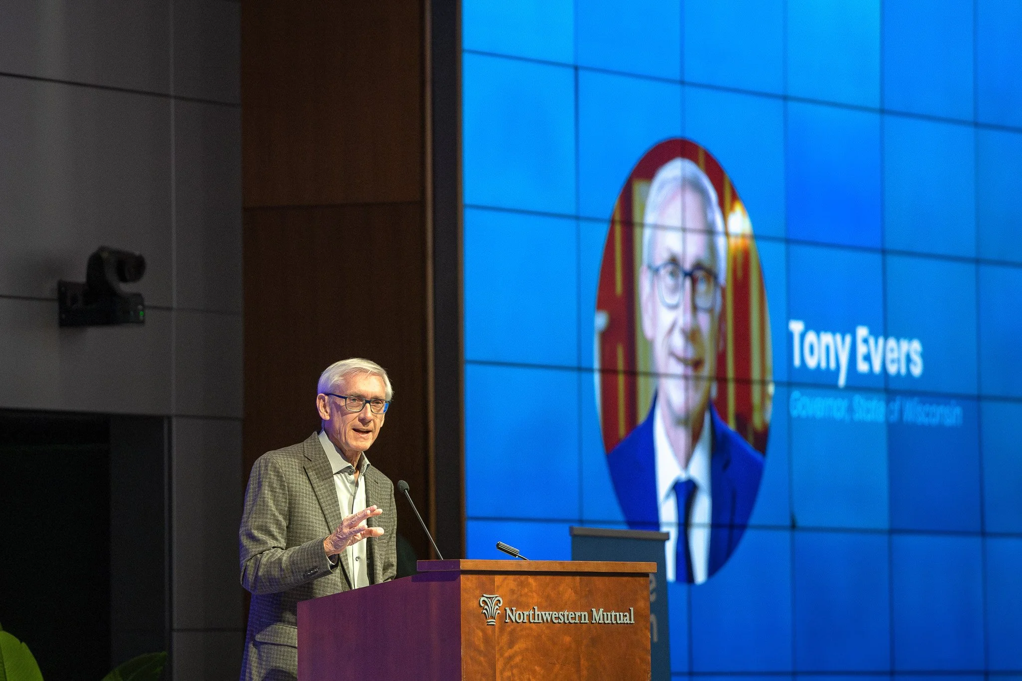 Wisconsin Governor Tony Evers speaks at a Northwestern Mutual podium, his name and portrait on the screen behind.