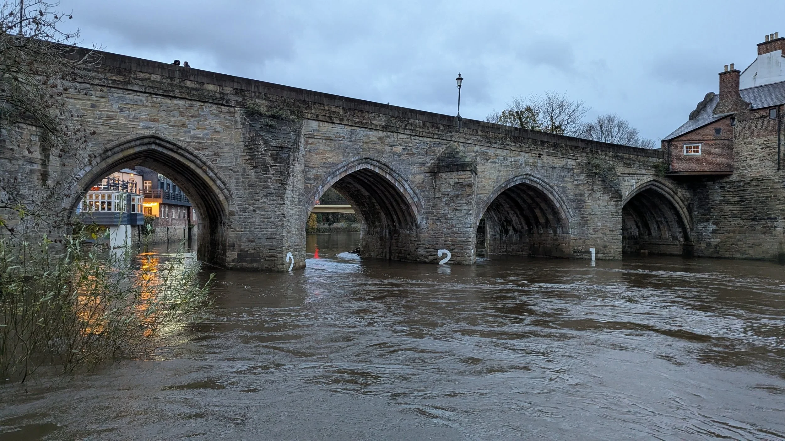 A view of Elvet Bridge with river water rising above the 2 white painted numbers on the bridge pillars