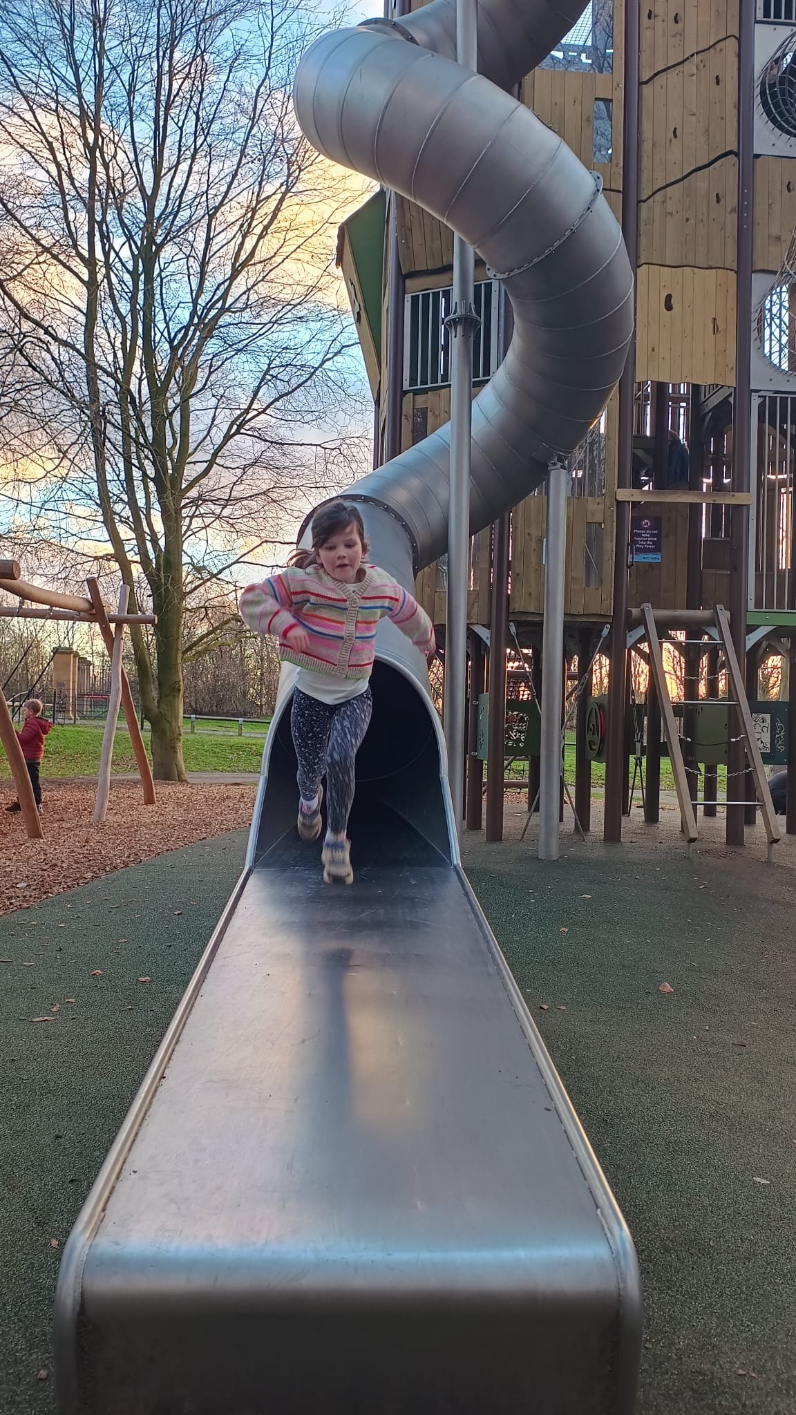 Child coming out of a metal slide attached to the tall play tower at Hardwick Park in Sedgefield.
