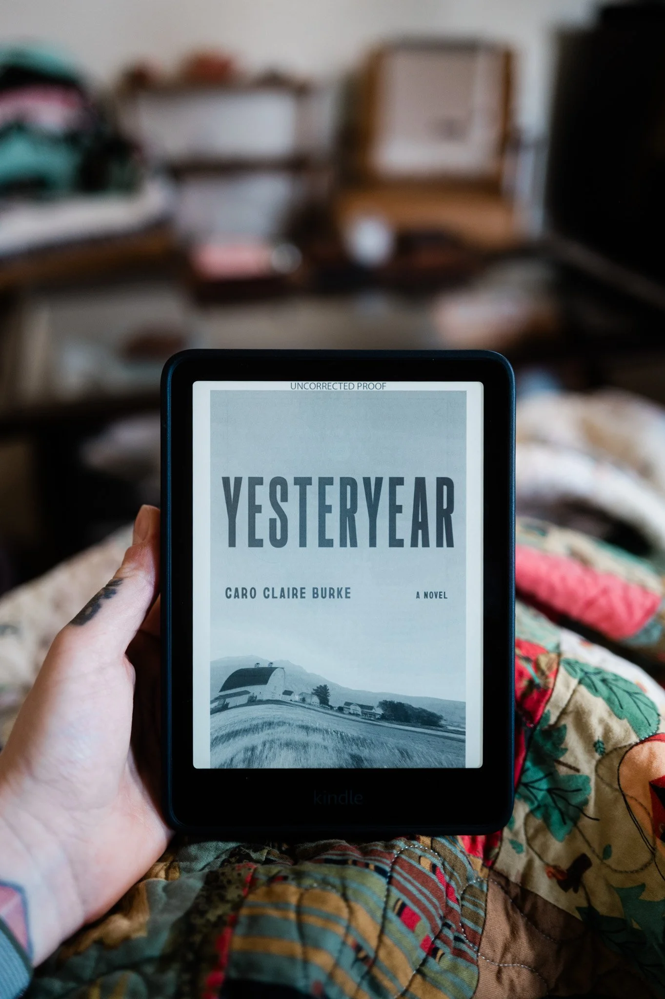 Advanced reader copy of Yesteryear by Caro Claire Burke displayed on the newest generation Kindle Paperwhite Signature with a blurred cozy interior background.