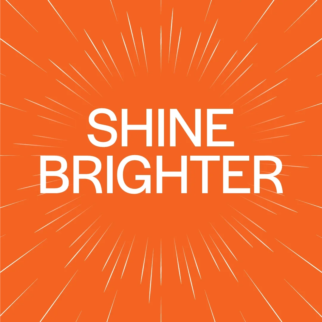 An image with a bright orange background. There is white text in the middle that says 'Shine Brighter'. Radiating outwards from the text are rays of light.